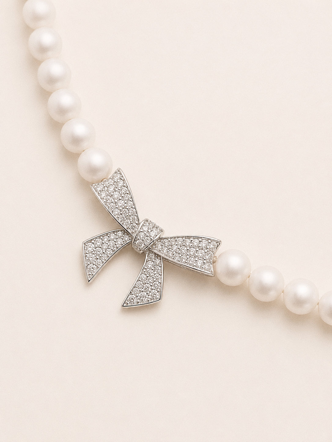 Angled view of the sparkling bow charm showing the crystal pavé ribbon detail against round white pearls