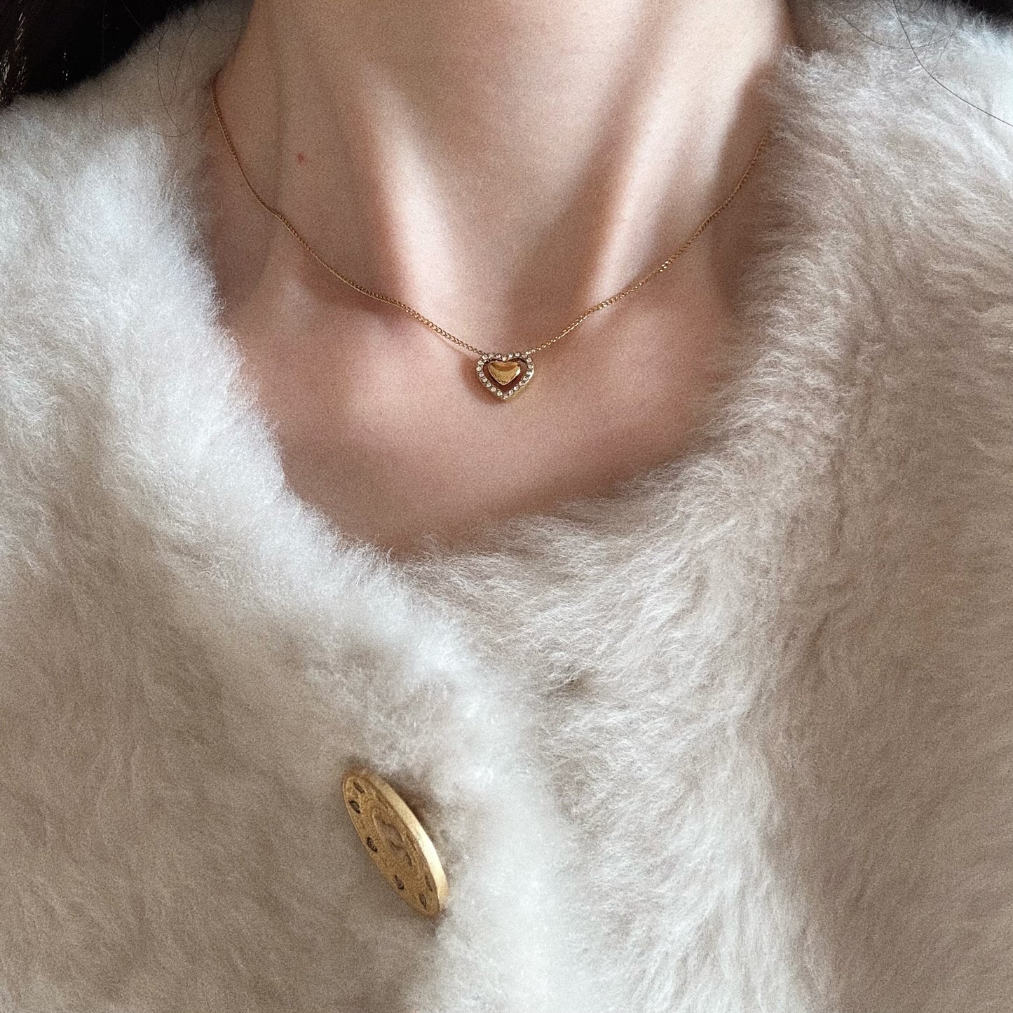 Woman wearing a dainty gold heart-within-a-heart necklace, styled for a romantic everyday look.