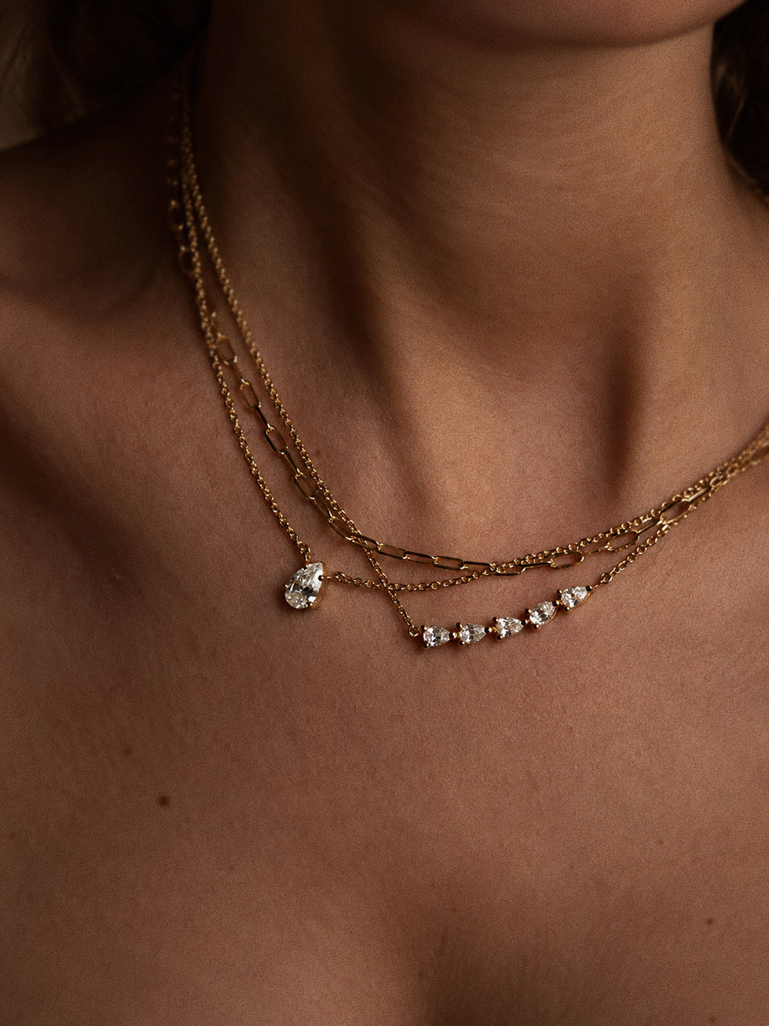 Linea paperclip chain worn as the upper layer alongside two finer necklaces with clear teardrop-shaped stones.