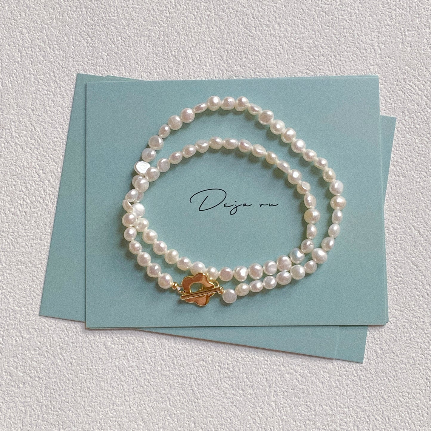 Freshwater pearl necklace with gold flower toggle clasp coiled on blue Deja vu jewellery card