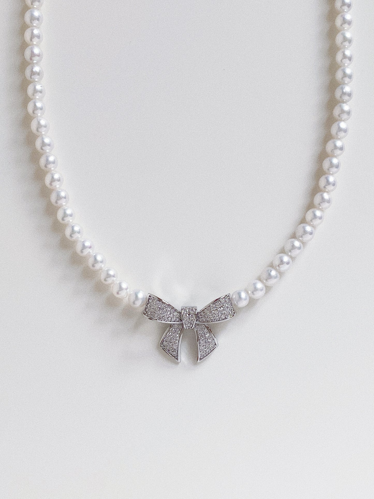 Macro detail shot of the pavé crystal bow charm centered on a strand of near-round natural pearls.