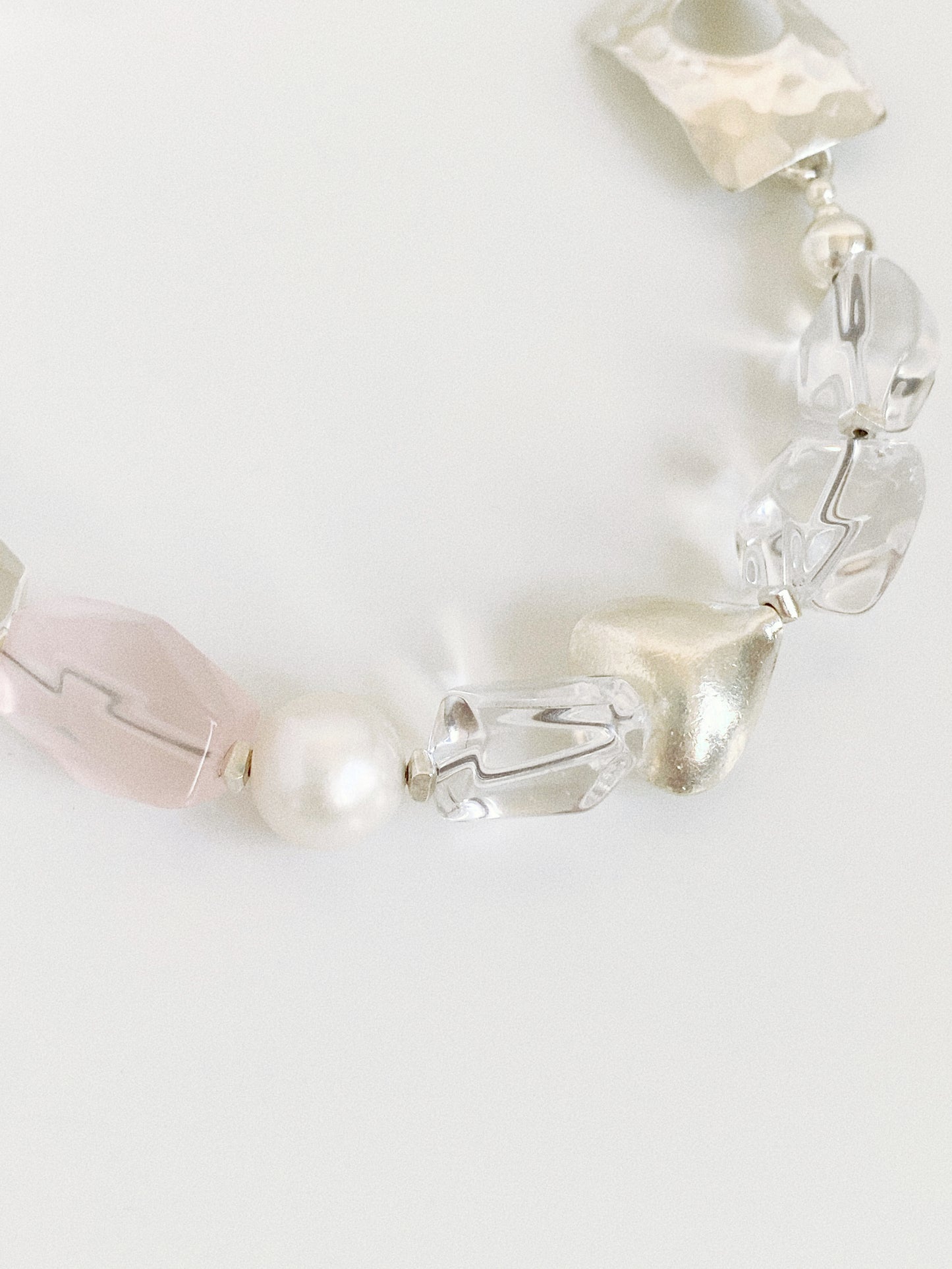 Close-up of the rose quartz nugget, freshwater pearl and brushed silver heart bead on a clear quartz bracelet