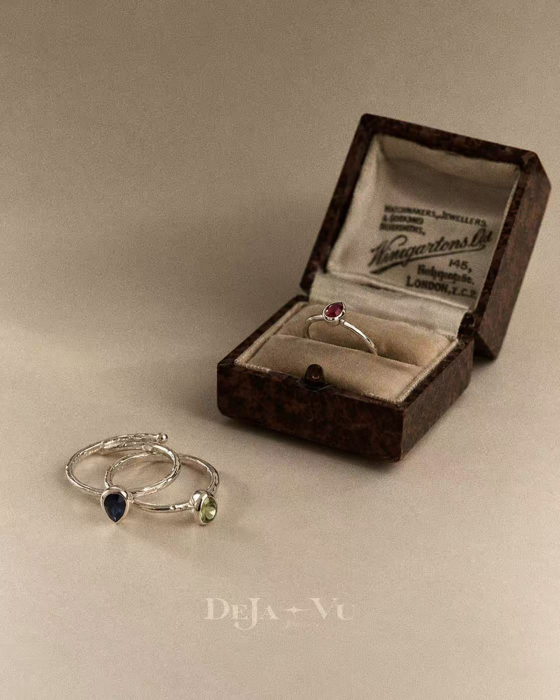Ruby teardrop ring displayed in a vintage-style jewellery box beside other gemstone rings; styling image