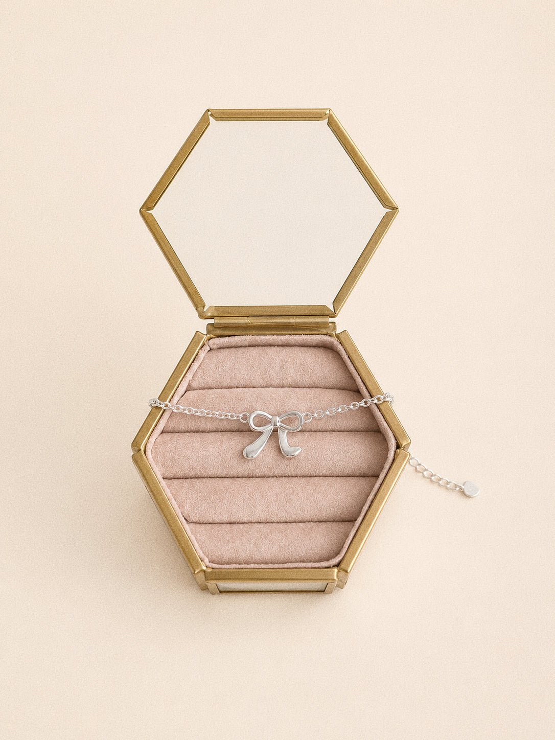 Ballet silver bow bracelet resting in a hexagonal glass and brass keepsake box with blush velvet rolls.