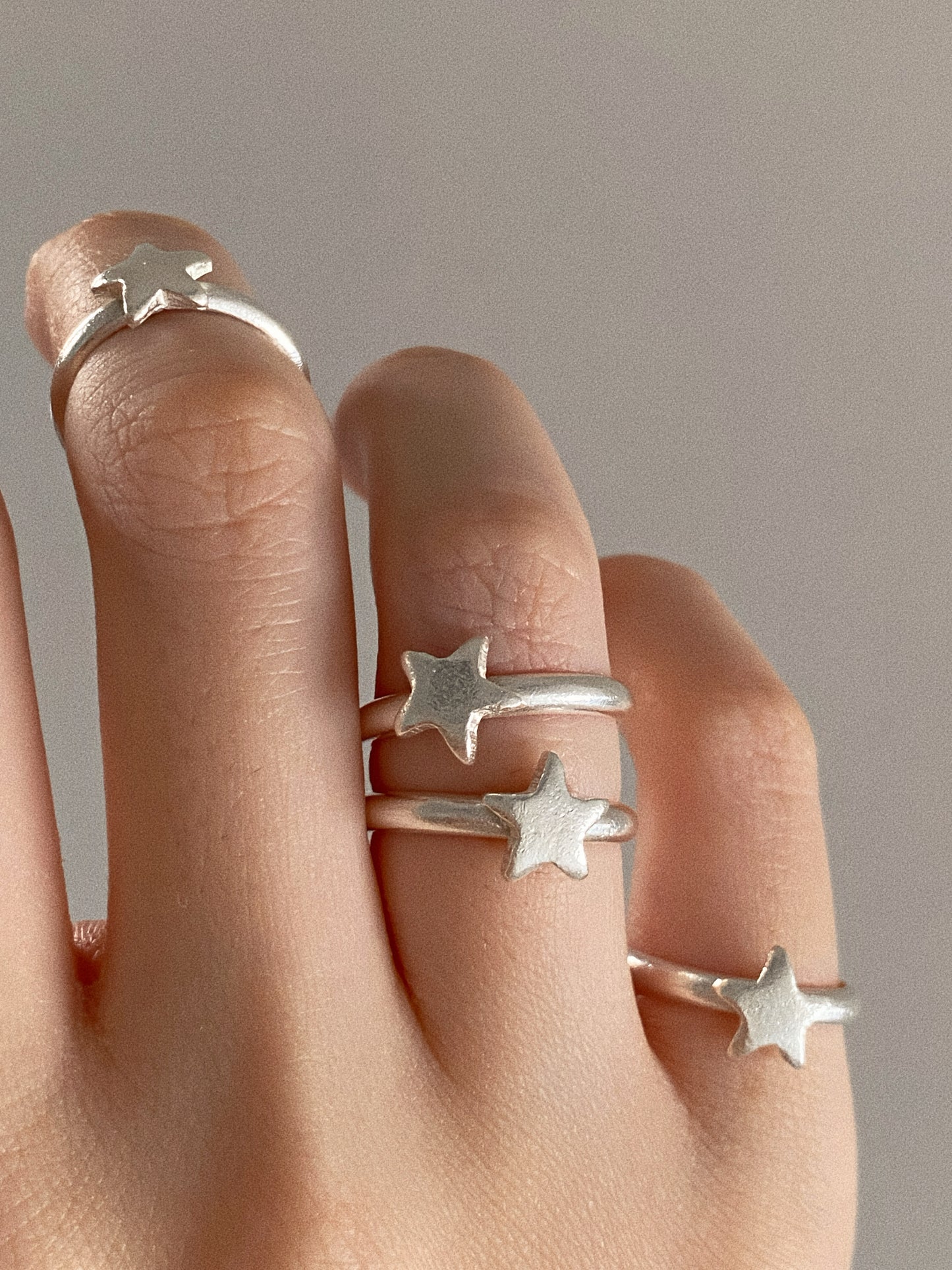 Four handmade sterling silver star rings stacked across one hand, each hand finished star slightly different.