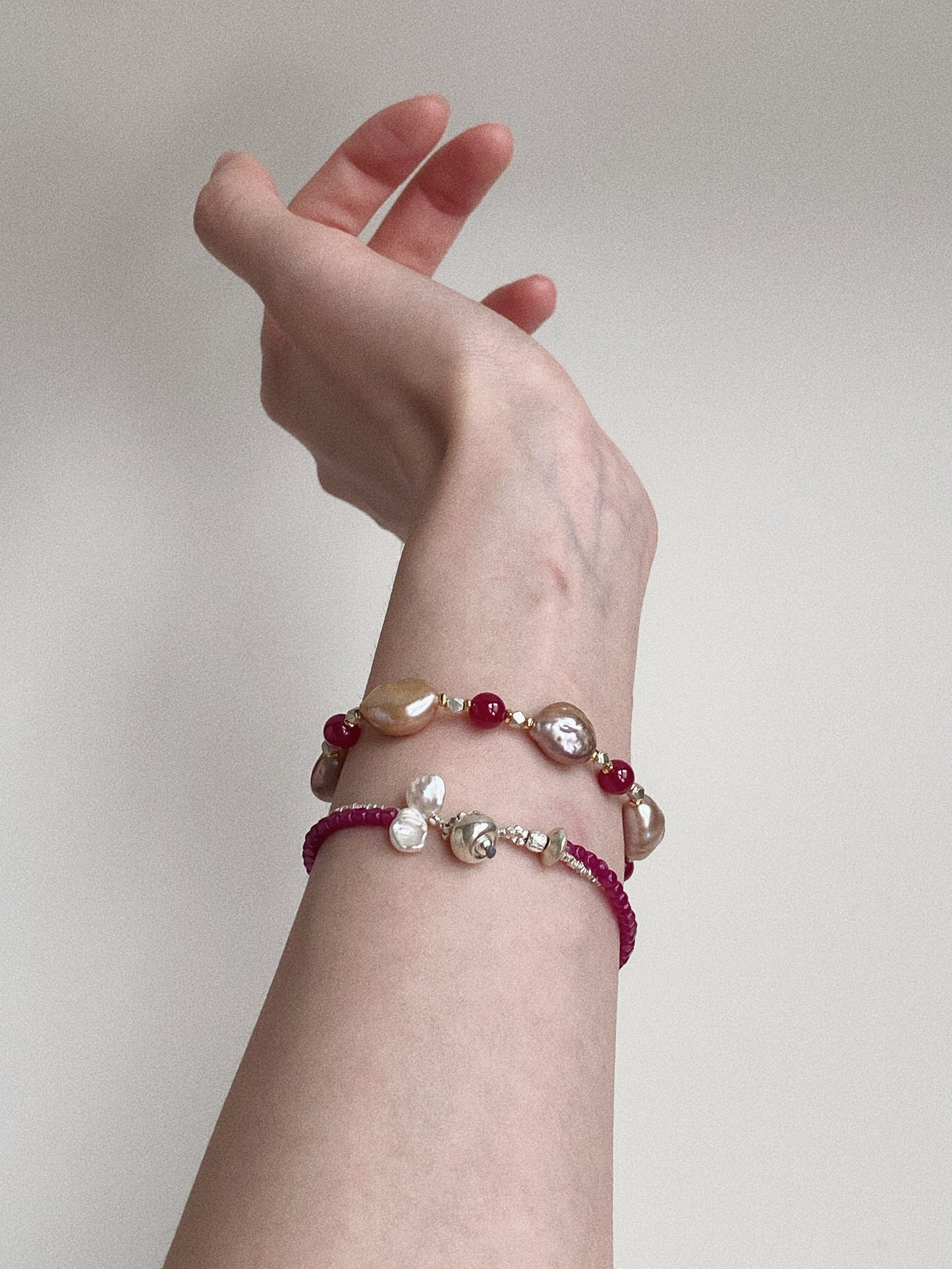 Lifestyle shot of a stacked wrist featuring the Roseate baroque pearl bracelet and a dainty ruby-toned beaded strand.