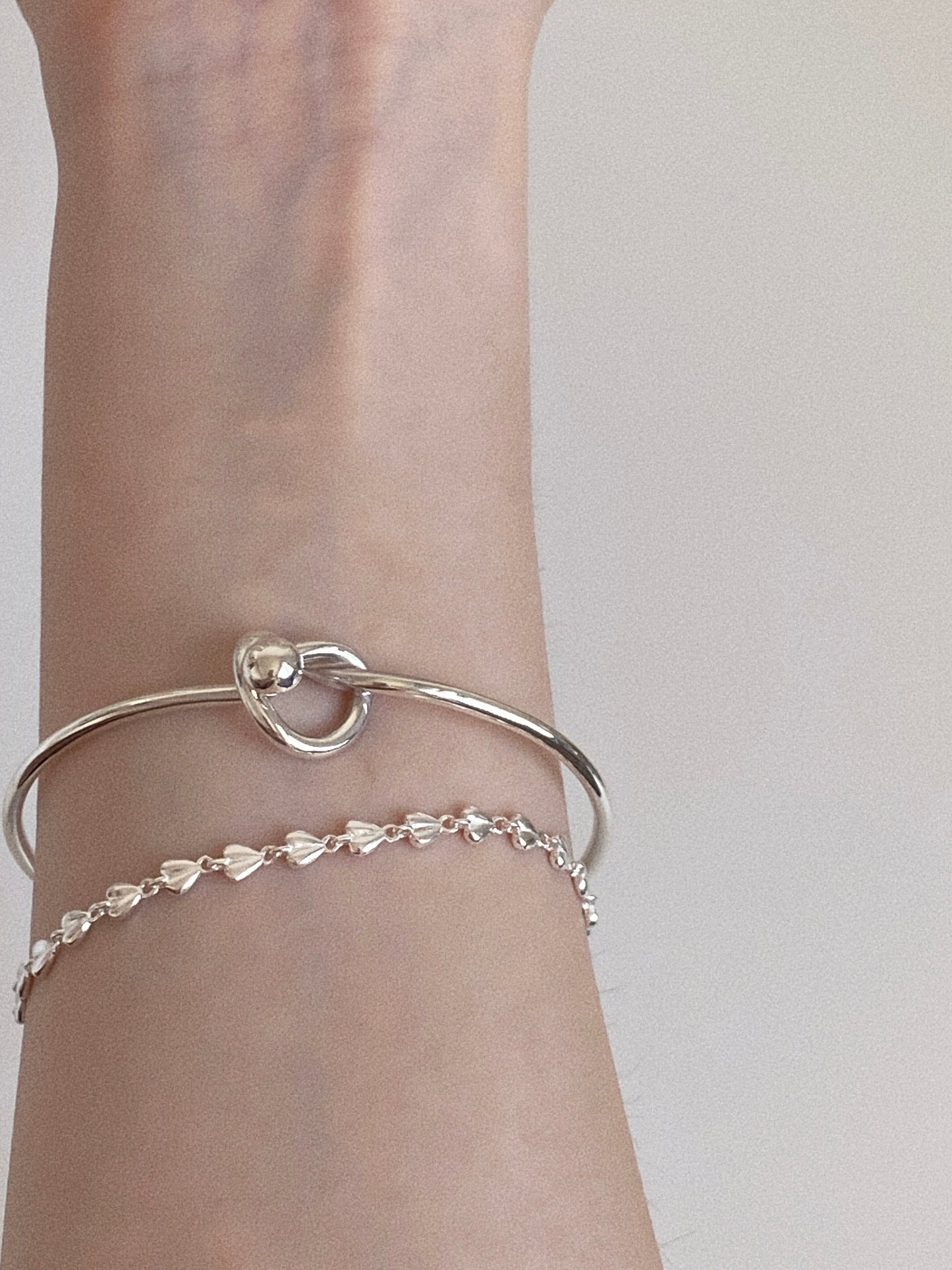 Sterling silver heart link bracelet layered with a silver love knot cuff bangle on the wrist
