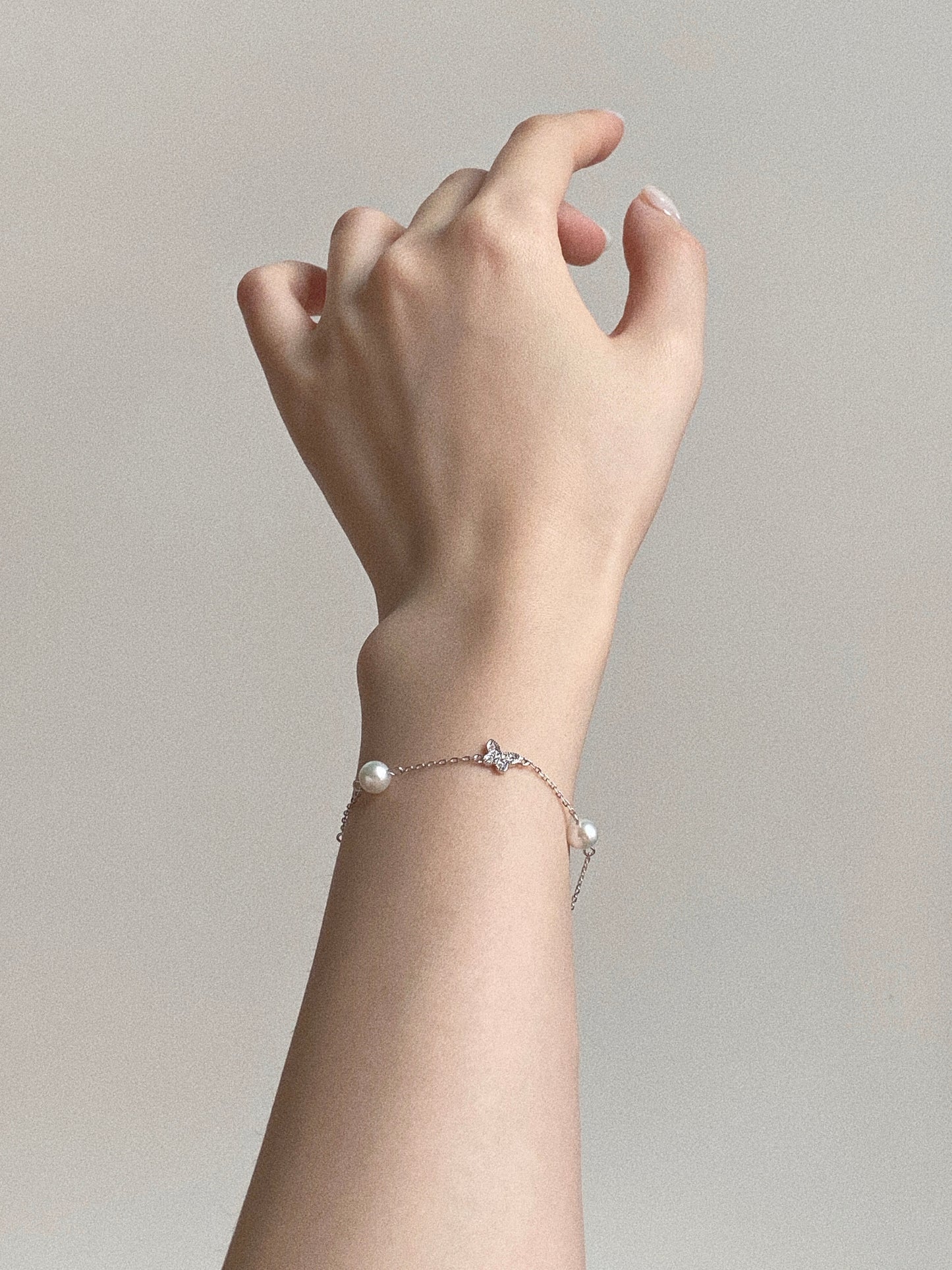 Aesthetic hand shot of the dainty 925 sterling silver chain bracelet, highlighting the floating pearl design and delicate butterfly detail.