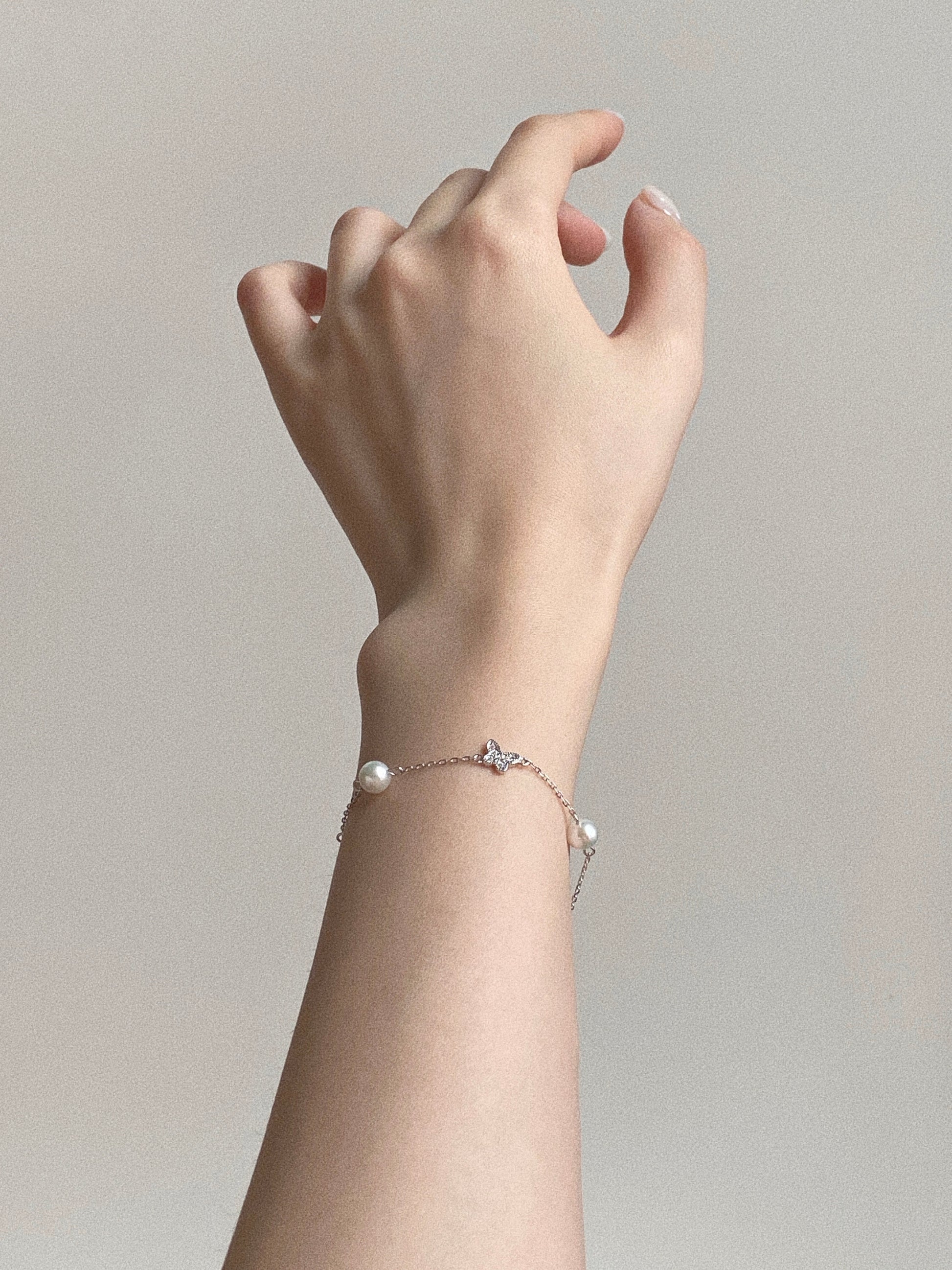 Aesthetic hand shot of the dainty 925 sterling silver chain bracelet, highlighting the floating pearl design and delicate butterfly detail.