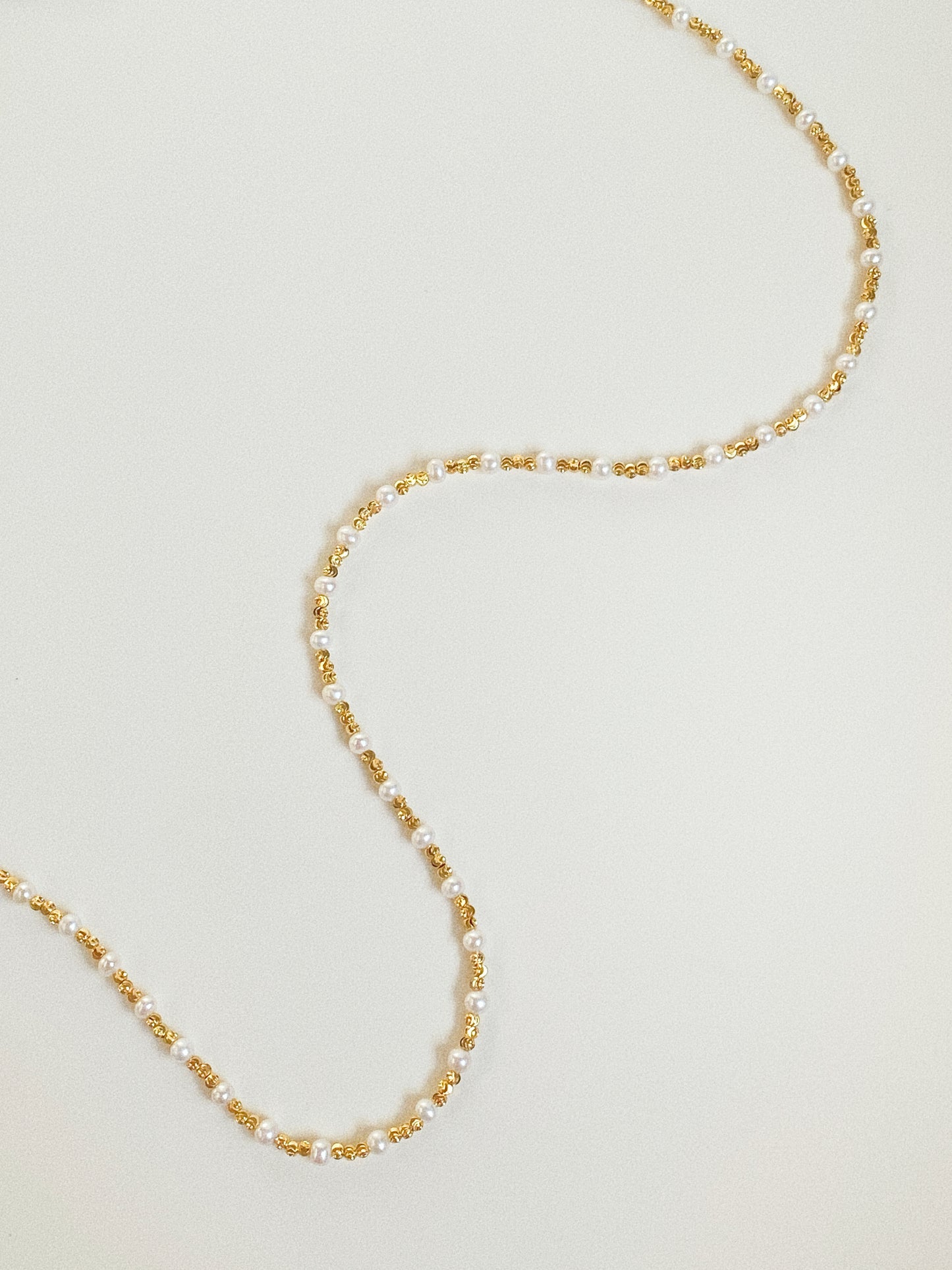 90cm long freshwater pearl and gold bead wrap necklace laid in S-curve flat lay