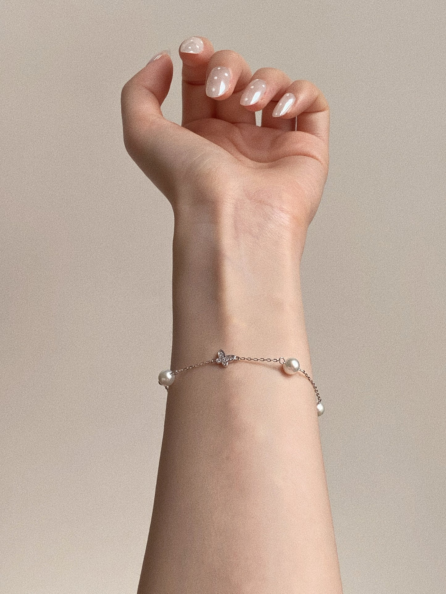 Model wearing the silver Mariposa Station Bracelet, clearly showing the crystal butterfly charm centered between natural freshwater pearls on the wrist.