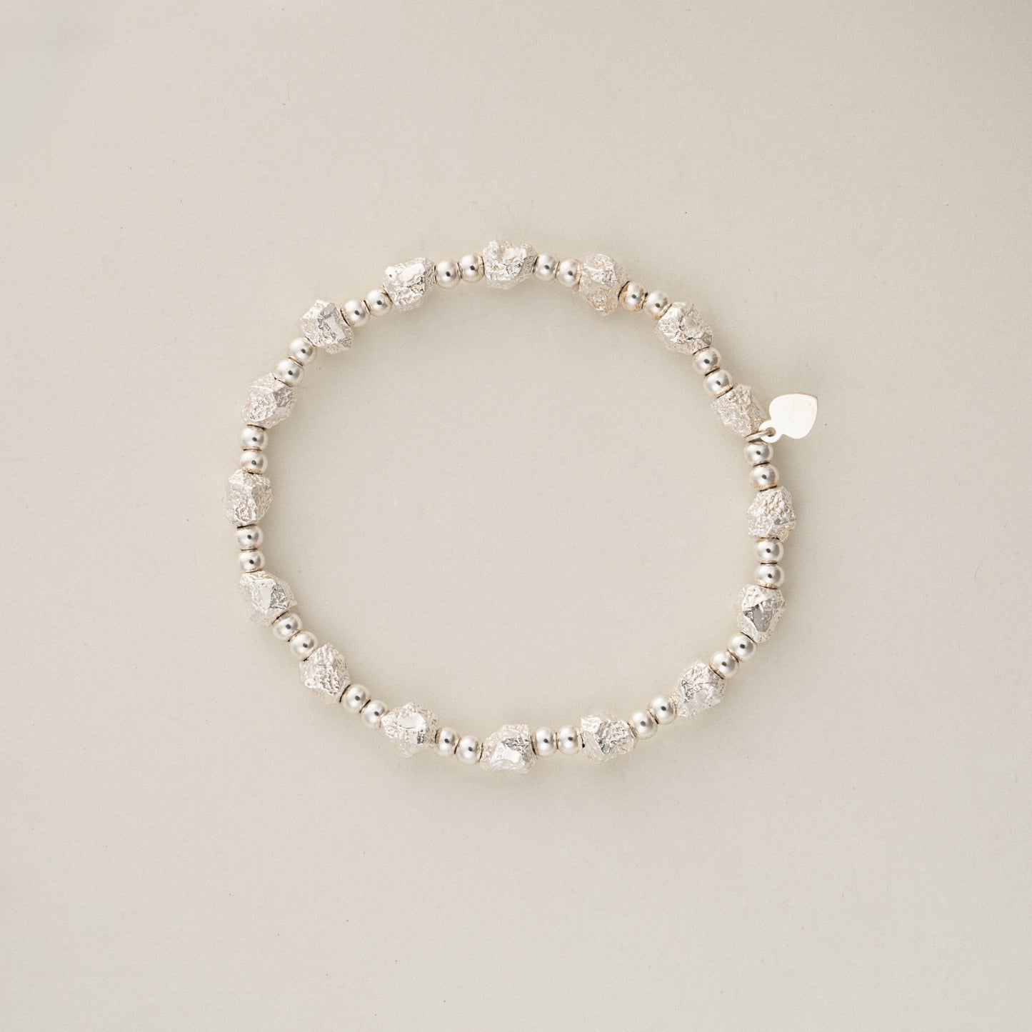 Direct top view flat lay of 11.5g solid sterling silver beaded bracelet, showing the elastic shape and signature S925 heart charm.