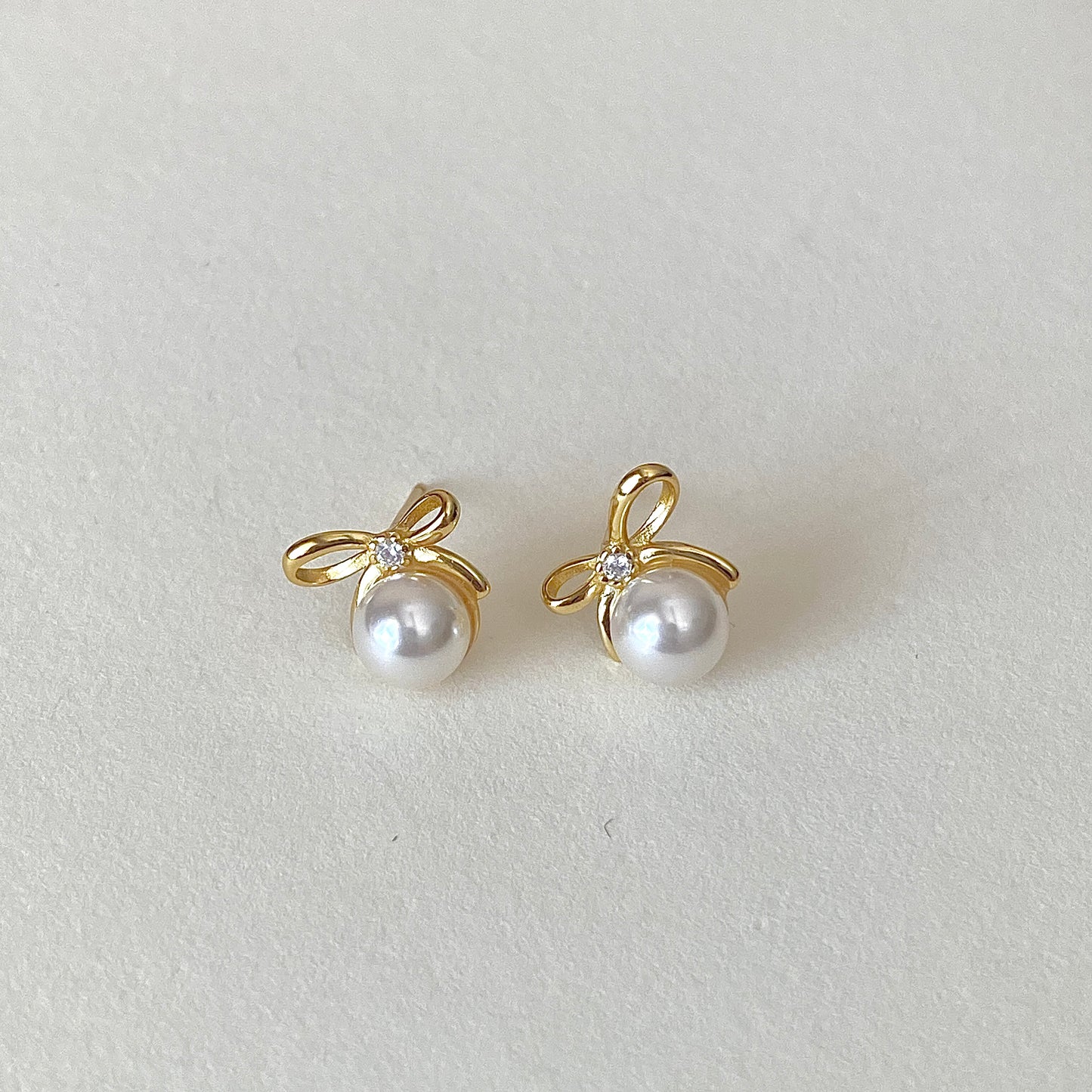 Gold bow ribbon pearl studs with tiny accent stone at knot, hypoallergenic posts