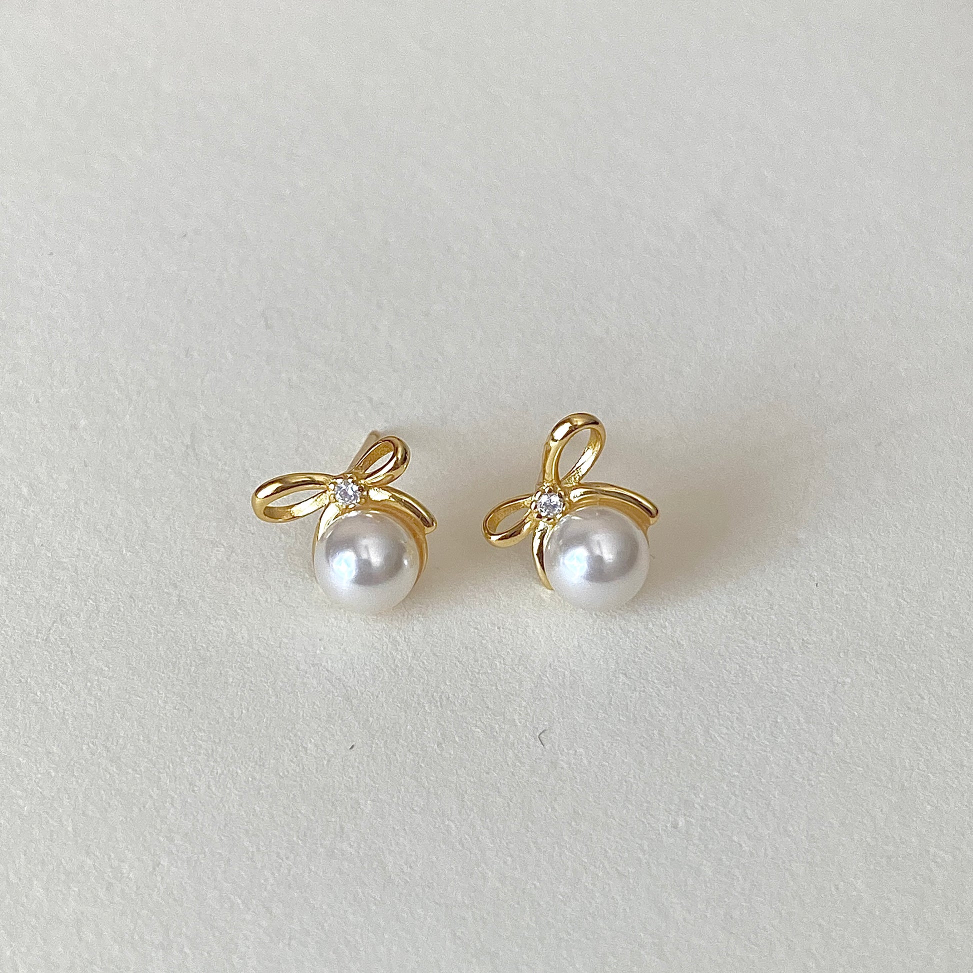 Gold bow ribbon pearl studs with tiny accent stone at knot, hypoallergenic posts