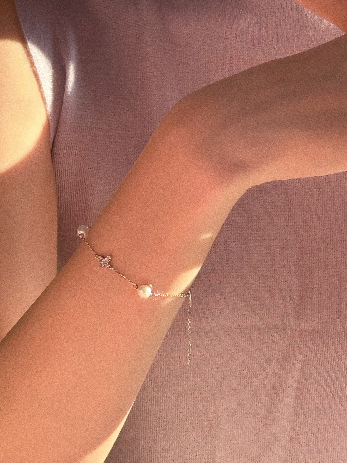 Sunlit lifestyle shot of the pearl and butterfly bracelet styled with a soft pink top, showing the extender chain and secure fit.