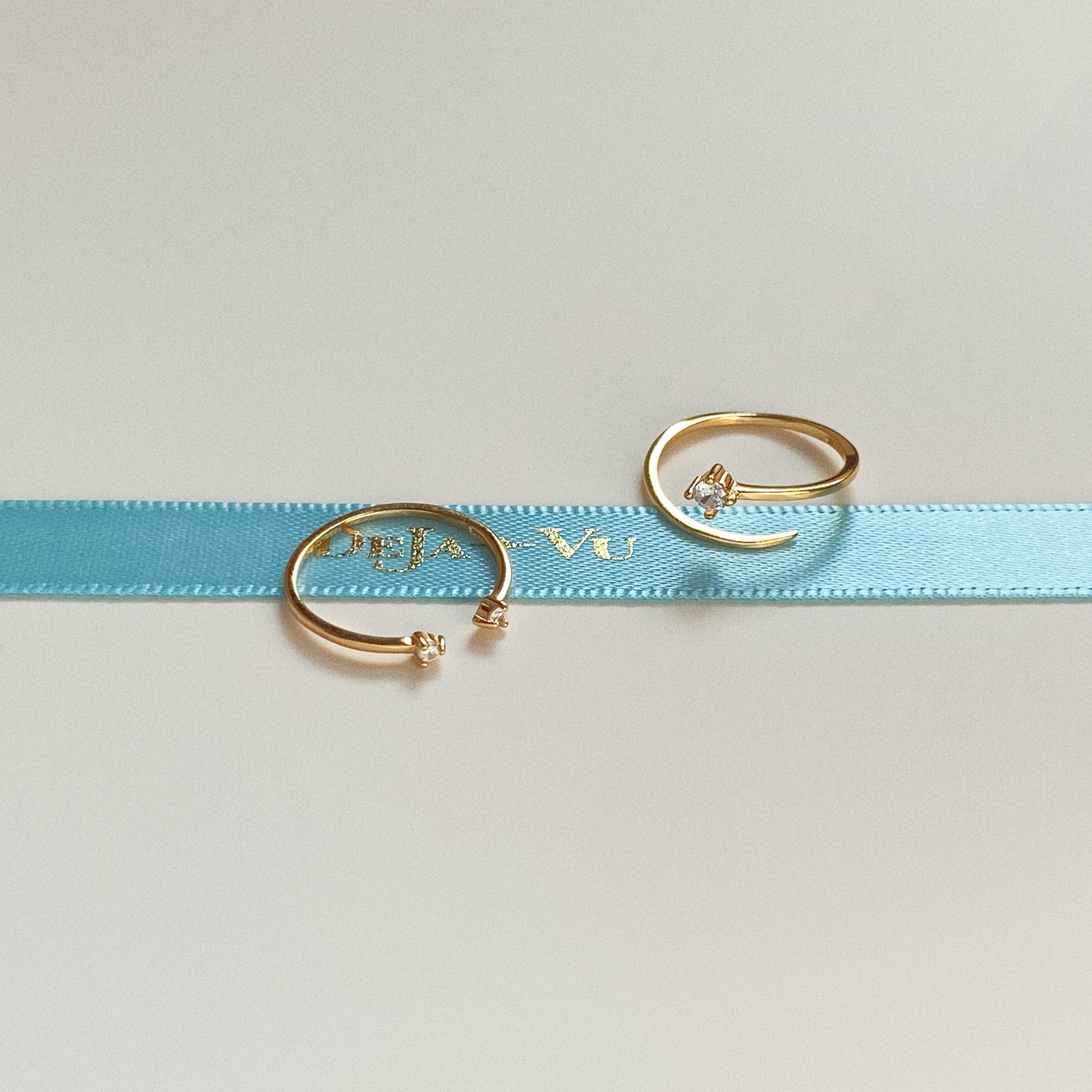 Two adjustable open gold pinky rings with single cubic zirconia resting on blue Deja vu Jewellery ribbon