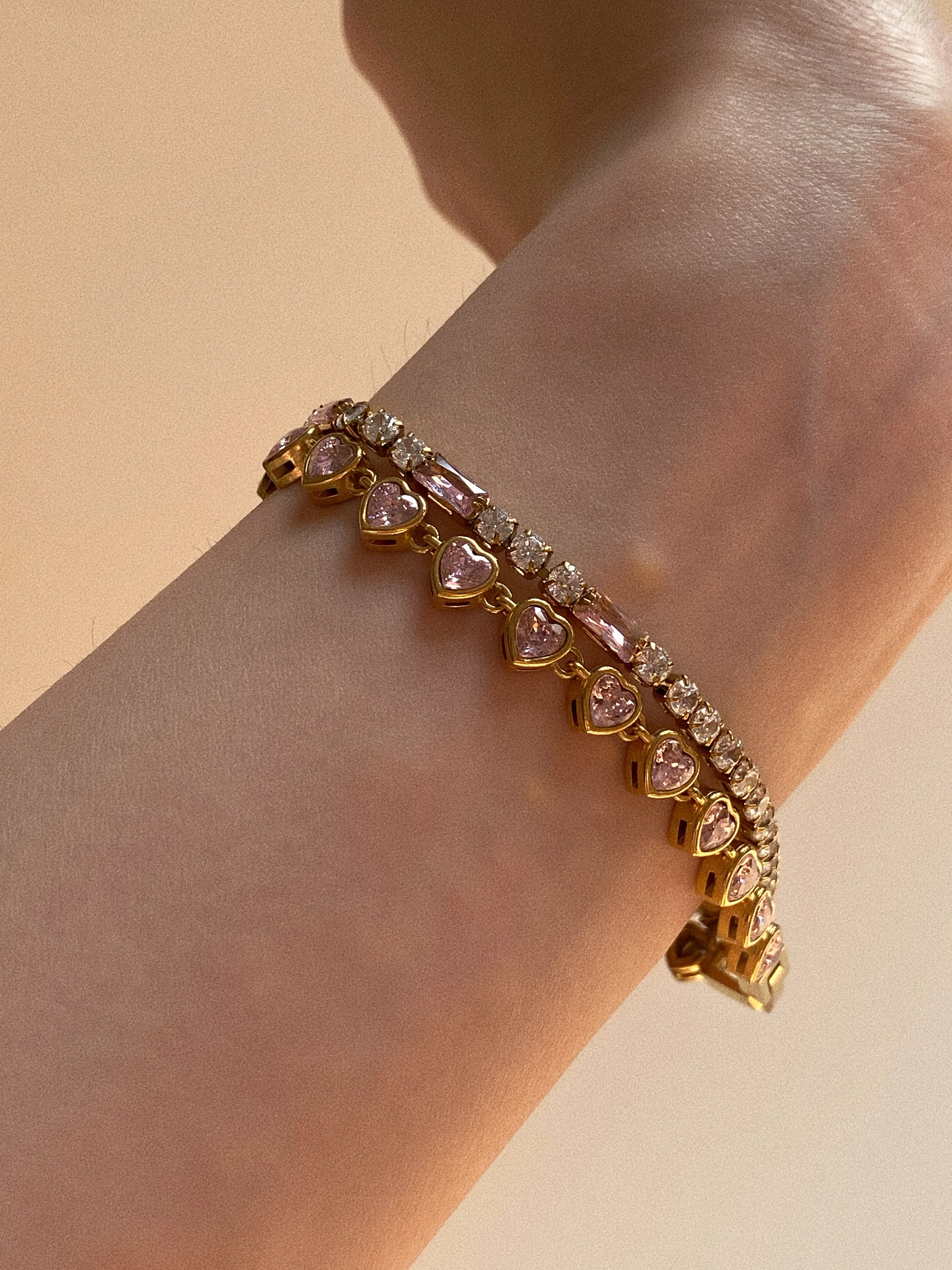 Model wearing pink heart tennis bracelet stacked with a mixed-cut crystal bracelet on wrist.