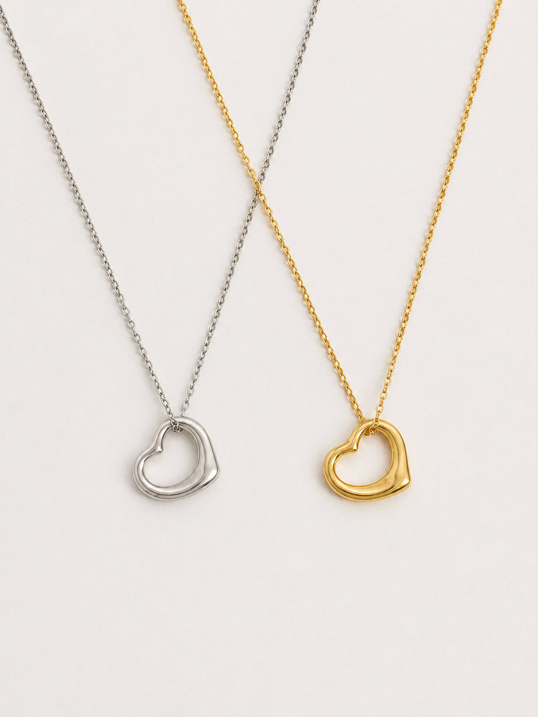 Silver and gold floating open heart pendant necklaces shown side by side, dainty 925 sterling silver heart necklaces in both finishes by Deja vu