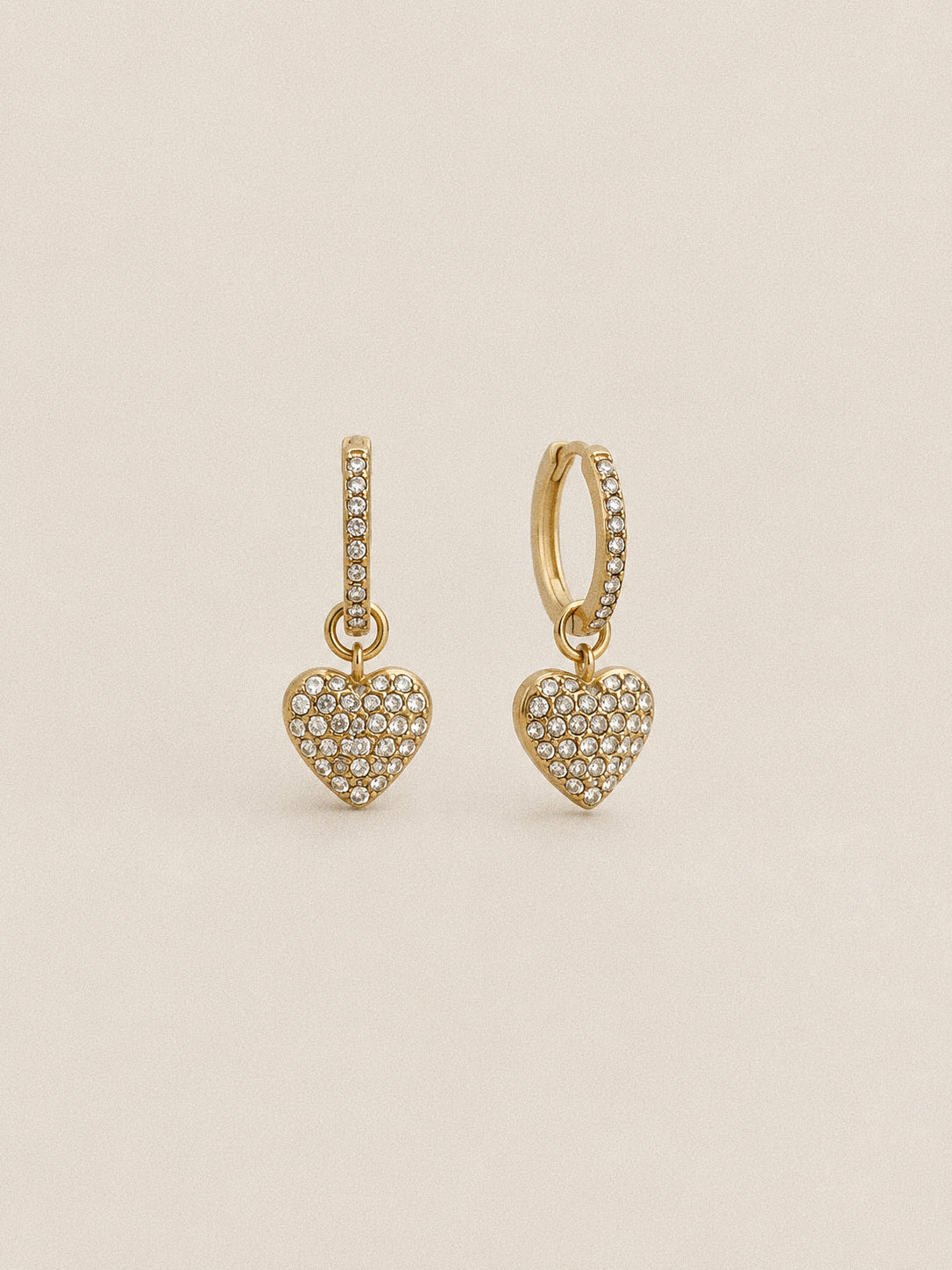 Pair of Amour gold-plated heart huggie hoop earrings with clear stones along the hoops and across the dangling heart charms.
