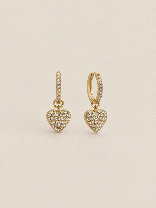 Pair of Amour gold-plated heart huggie hoop earrings with clear stones along the hoops and across the dangling heart charms.