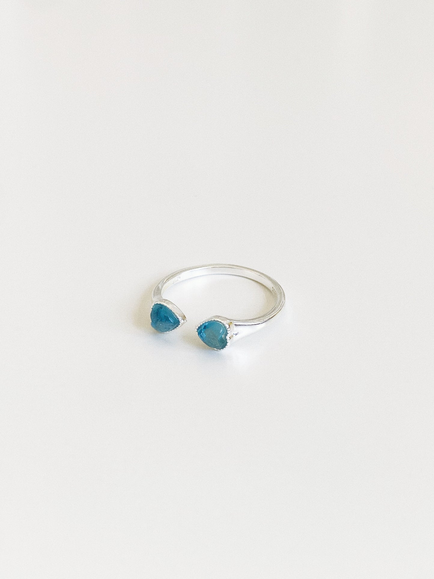 Angled view of an open band aquamarine ring showing the two blue heart-cut stones and slim polished silver band