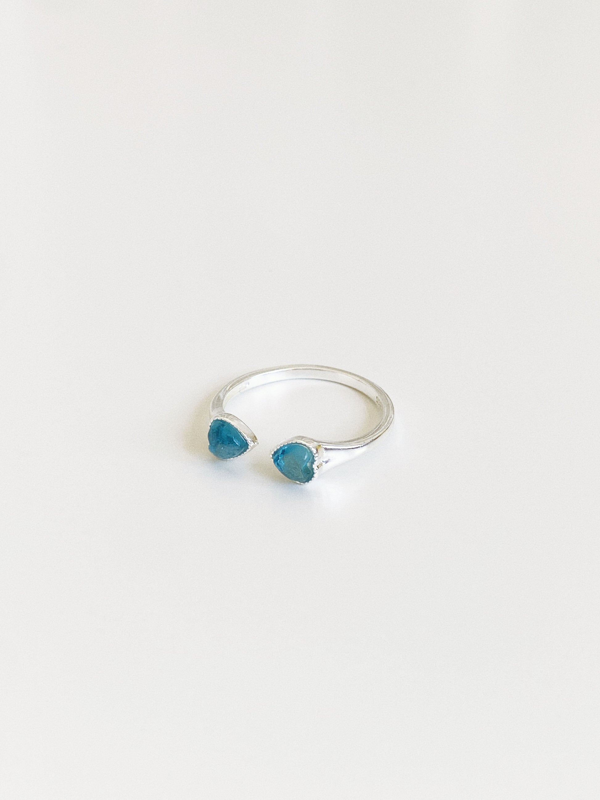 Angled view of an open band aquamarine ring showing the two blue heart-cut stones and slim polished silver band