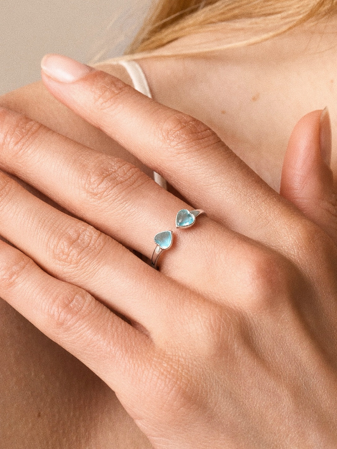 Model wearing the adjustable aquamarine double heart ring in sterling silver, two blue hearts meeting across the open band