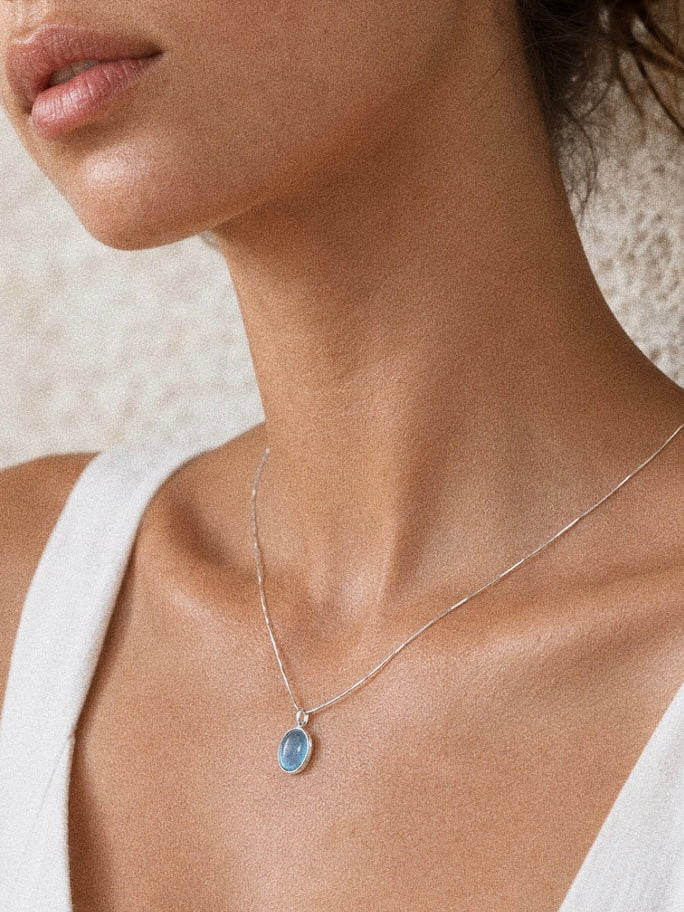 Model in a white linen top wearing the aquamarine cabochon pendant necklace at the base of the throat in warm light