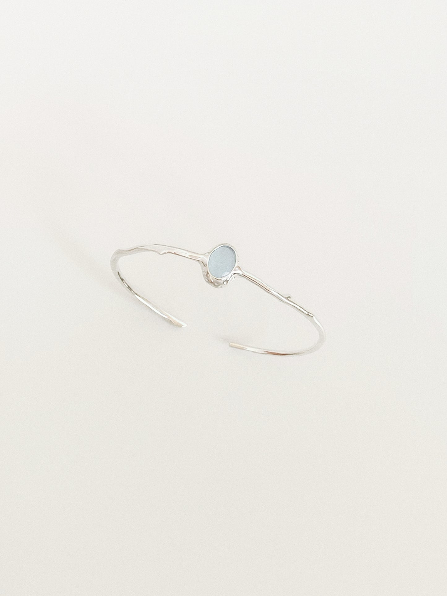 Open silver cuff bangle with oval aquamarine stone photographed on a neutral background