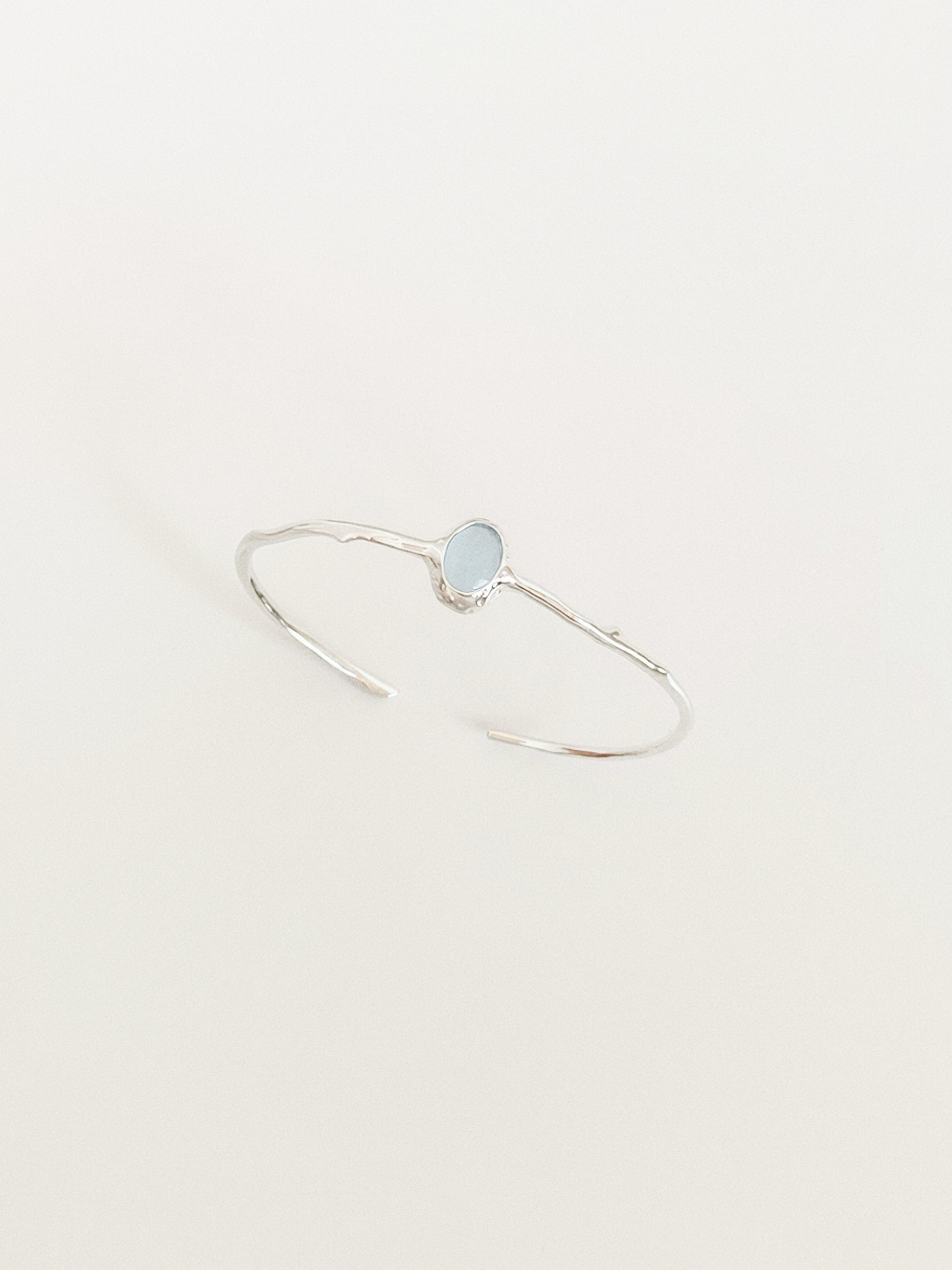 Open silver cuff bangle with oval aquamarine stone photographed on a neutral background