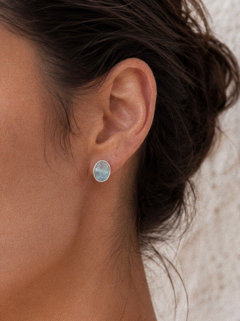 Close-up of a model wearing a natural aquamarine oval cabochon stud earring in a textured silver bezel