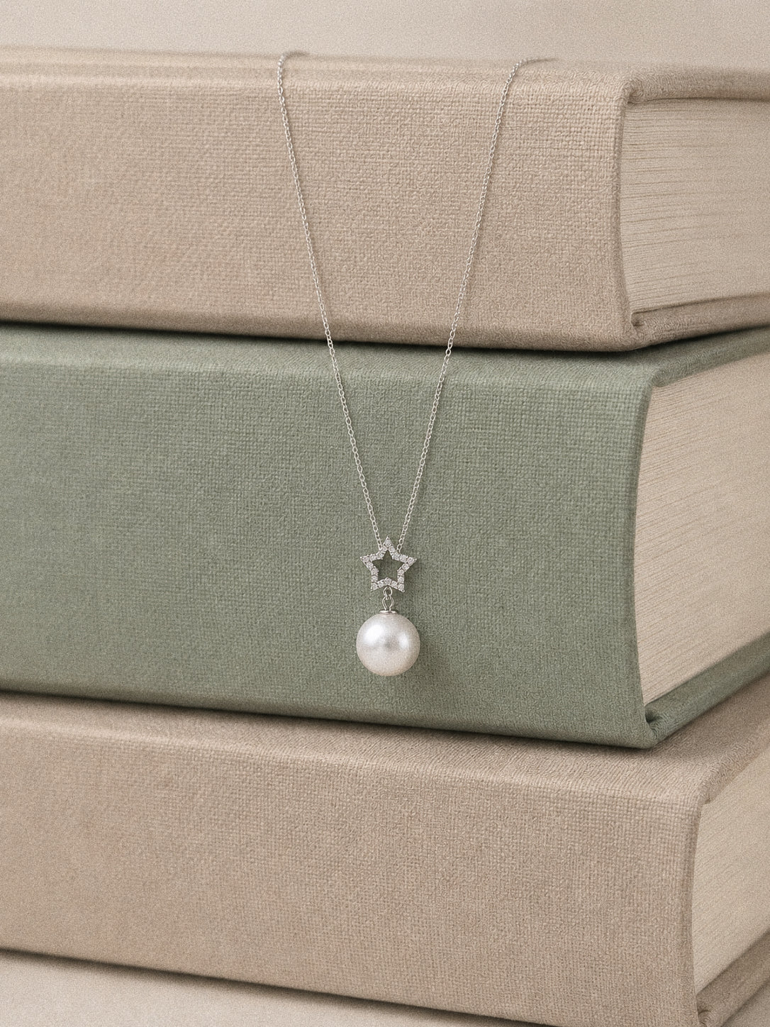 Astra star and Edison pearl Y necklace arranged over stacked sage green and oatmeal-coloured books.