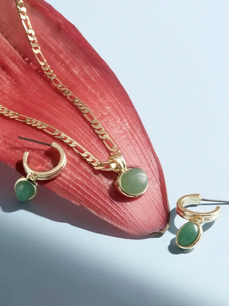 A matching jewelry set featuring a natural aventurine necklace and earrings laid on a red tropical leaf.