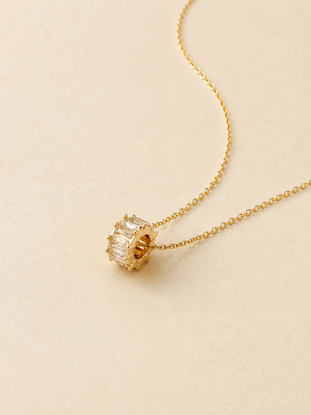 Macro close-up of a gold spinning wheel charm set all around with clear baguette cut cubic zirconia on a dainty chain