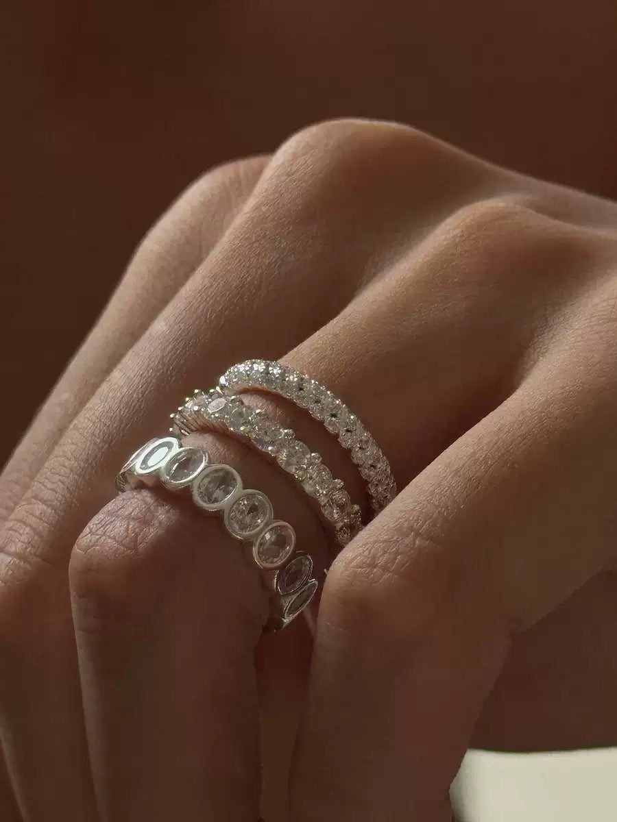 Hand wearing layered sterling silver bands with round cubic zirconia.