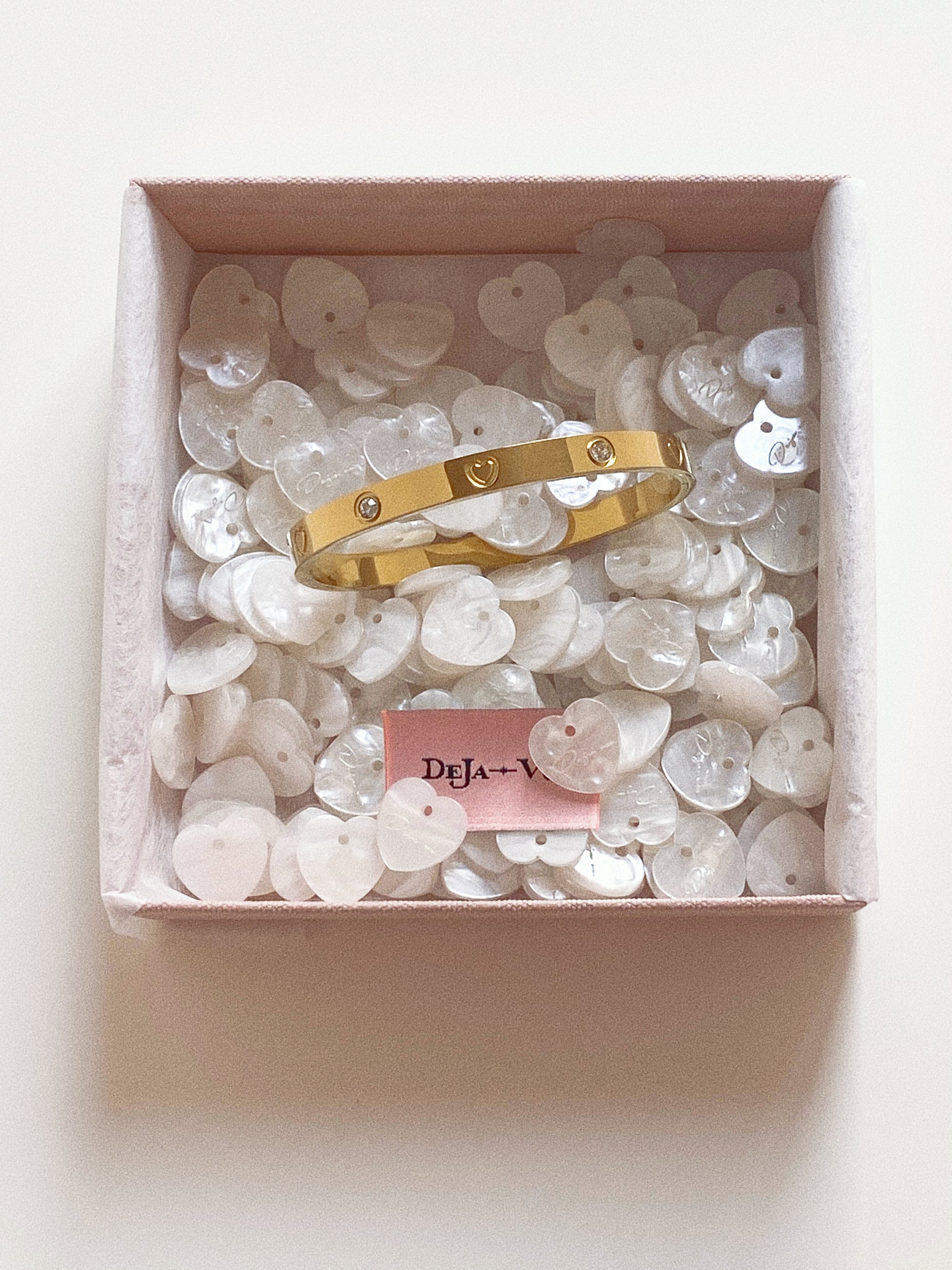 Gold rigid bangle bracelet featuring etched hearts and crystals, displayed in a luxury box with mother-of-pearl shells.
