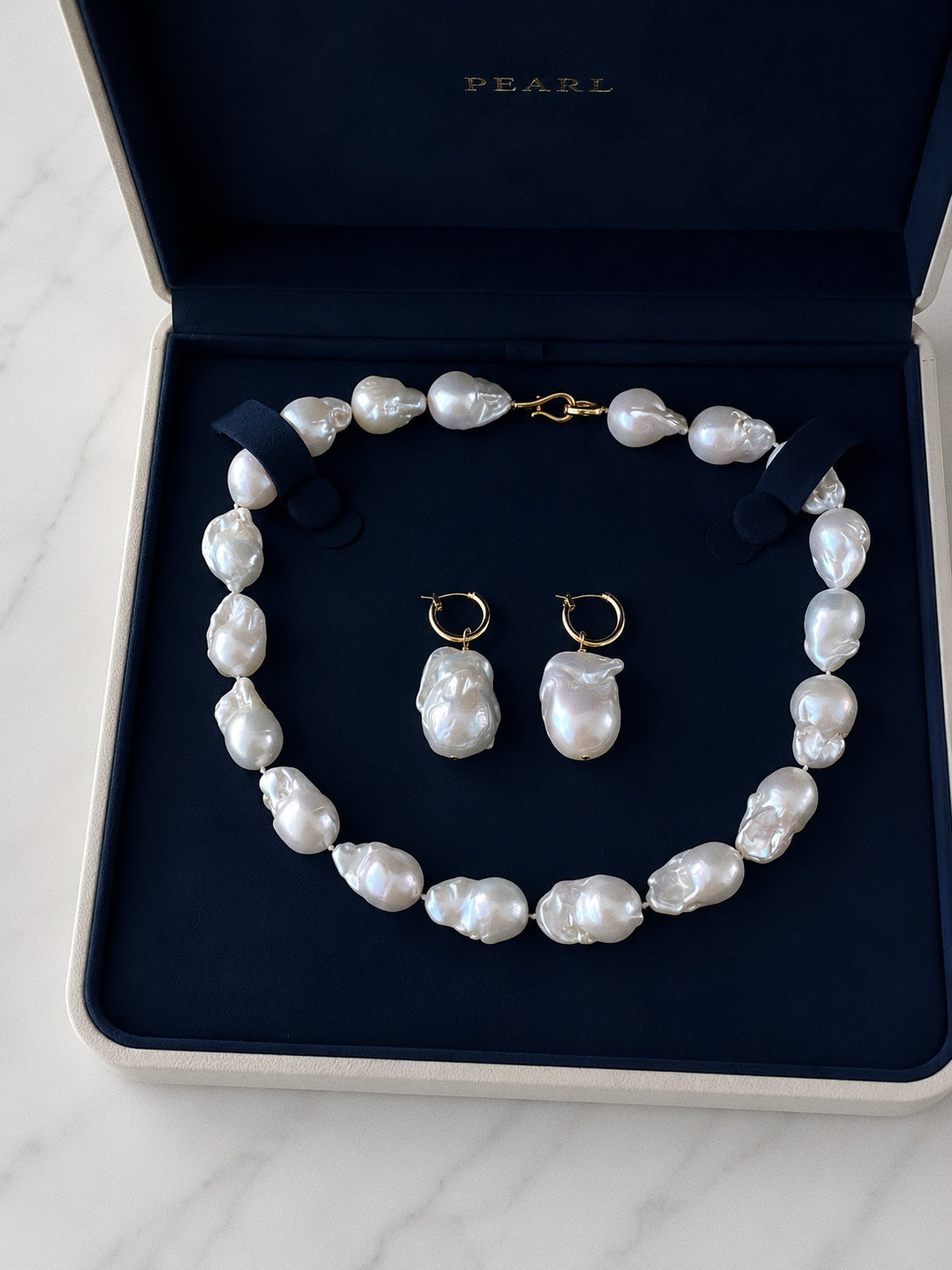 Large baroque pearl necklace and matching gold hoop pearl drop earrings presented in a navy jewellery box