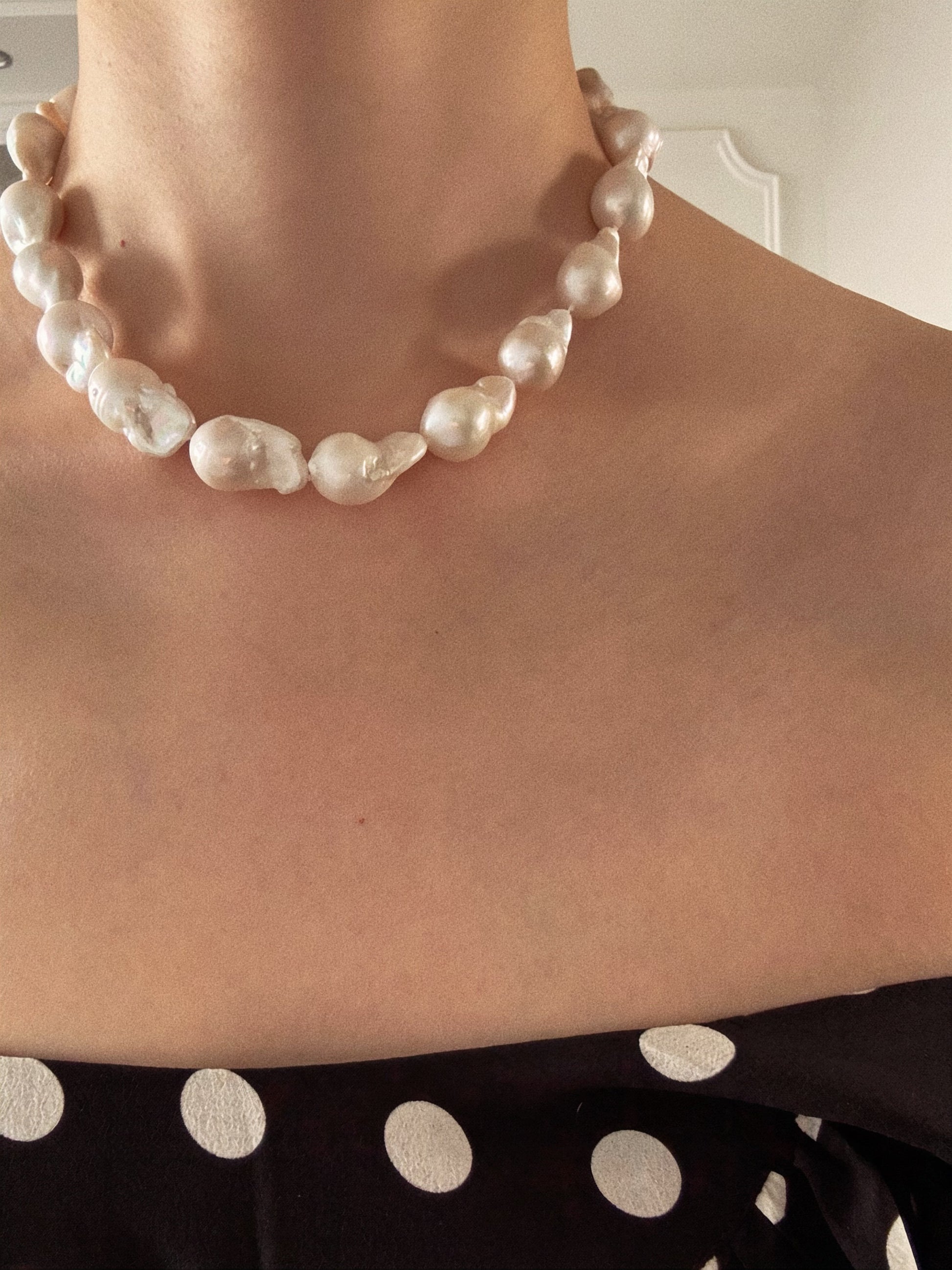 Model wearing a statement strand of large white fireball baroque pearls at the collarbone with a white strapless dress