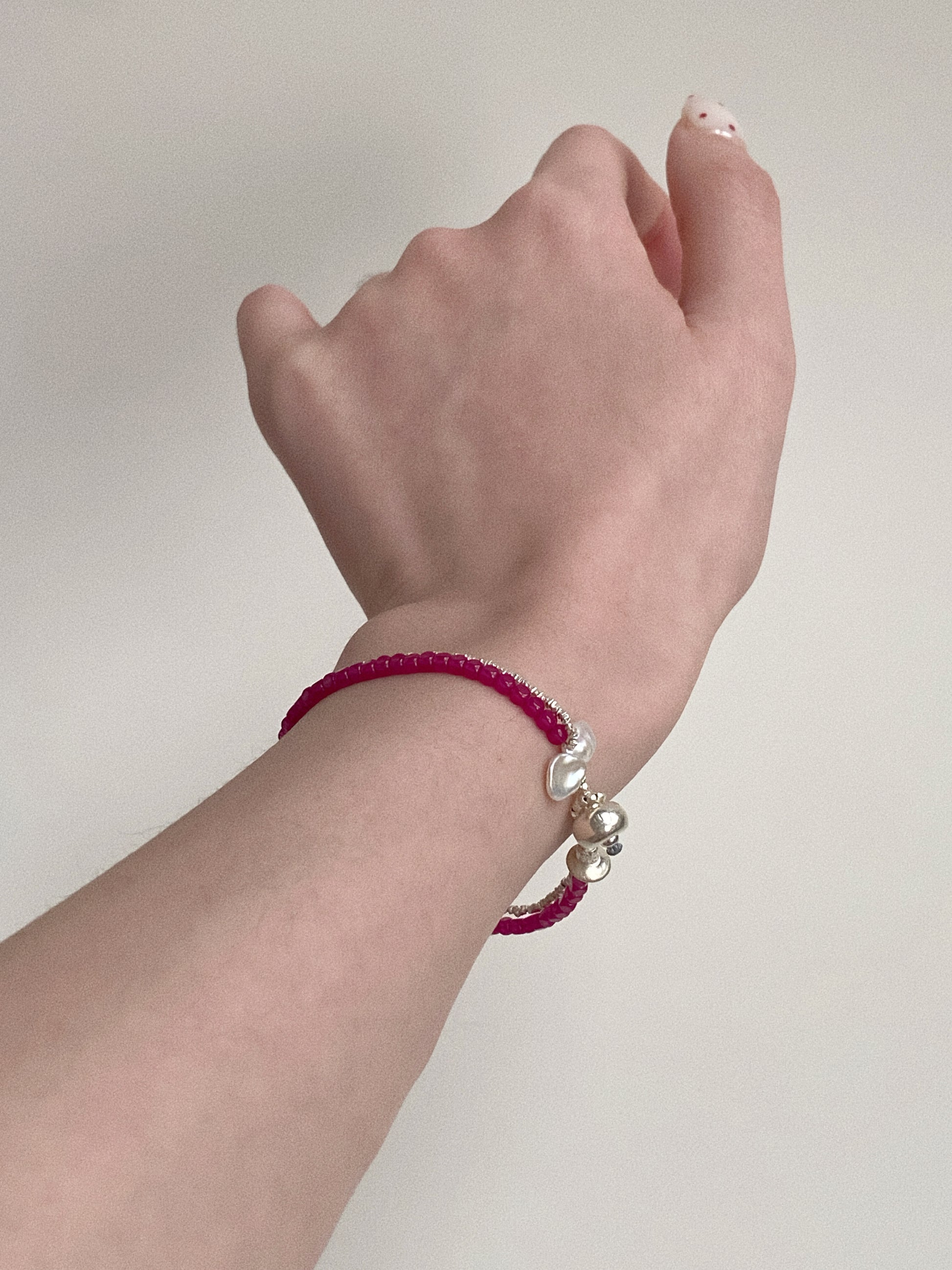 Detailed shot of the baroque petal pearls and silver charm closure on a red ruby beaded bracelet.