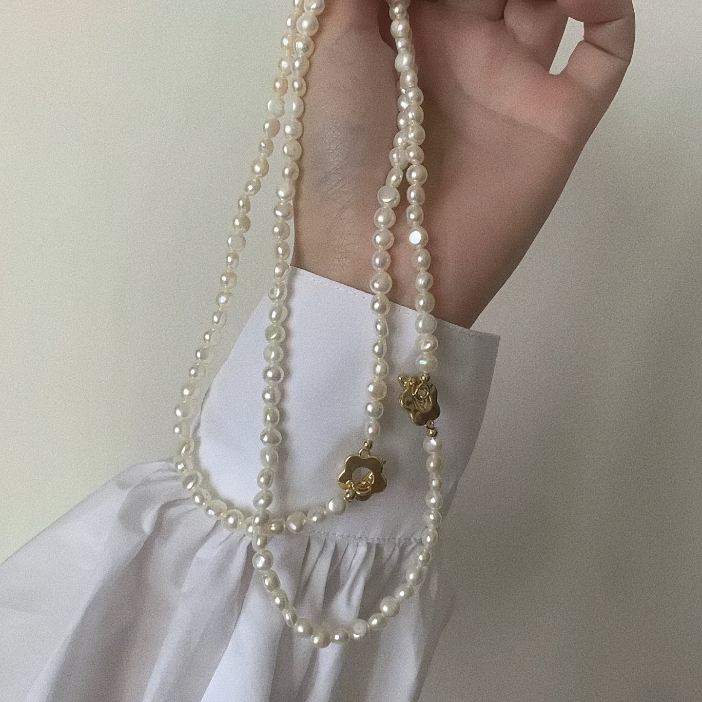 Hand holding two lengths of freshwater baroque pearl necklaces showing gold flower toggle clasps