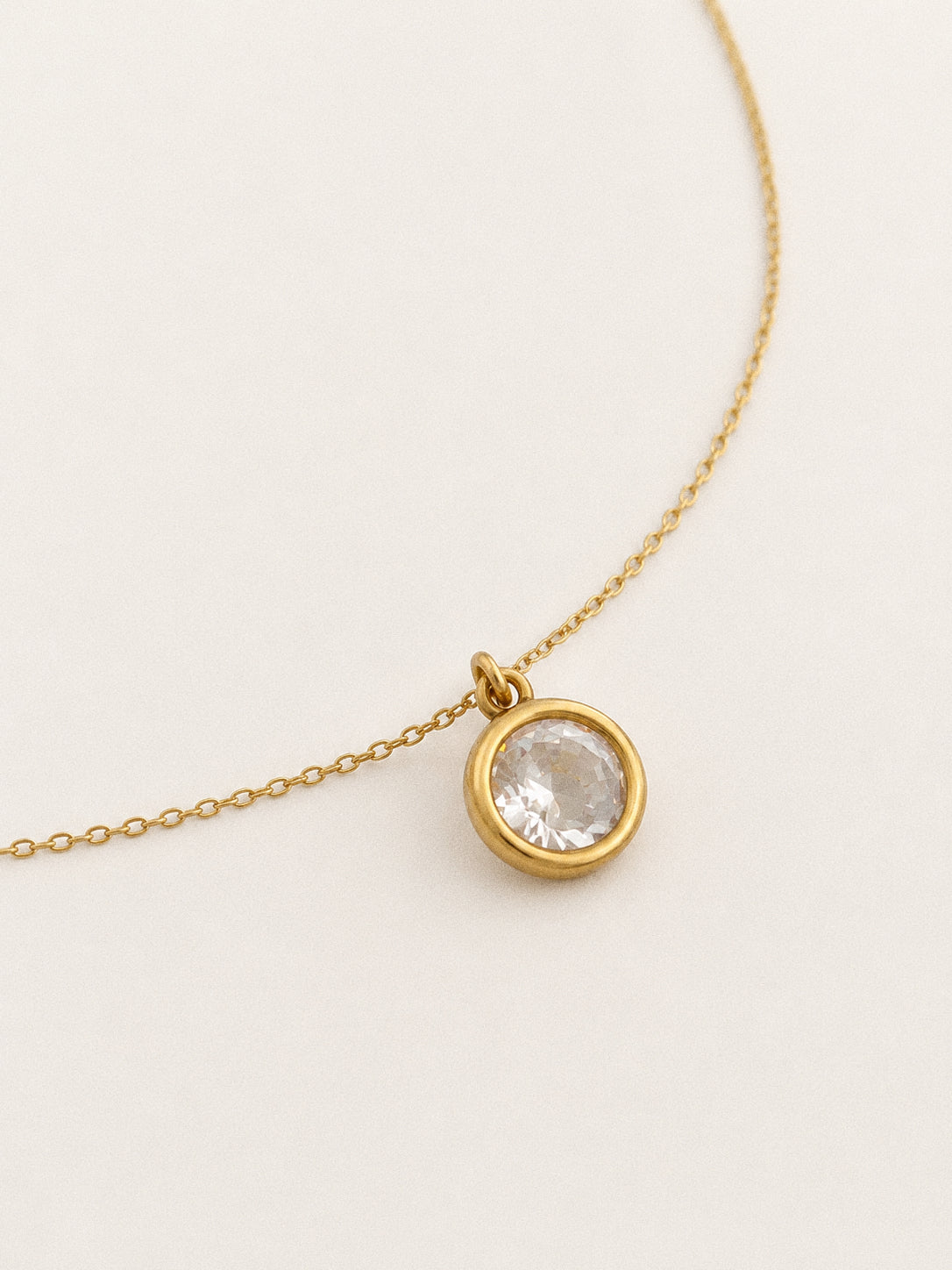 Round cubic zirconia pendant in a smooth 18k gold bezel setting on a delicate cable chain