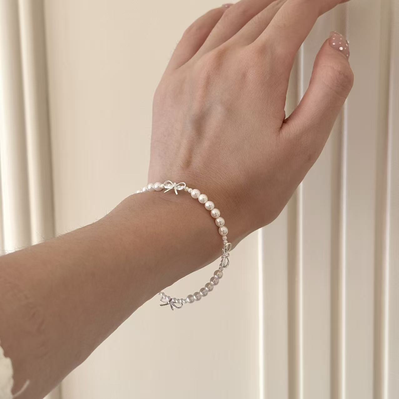 pearl bracelet with silver bow charms on wrist