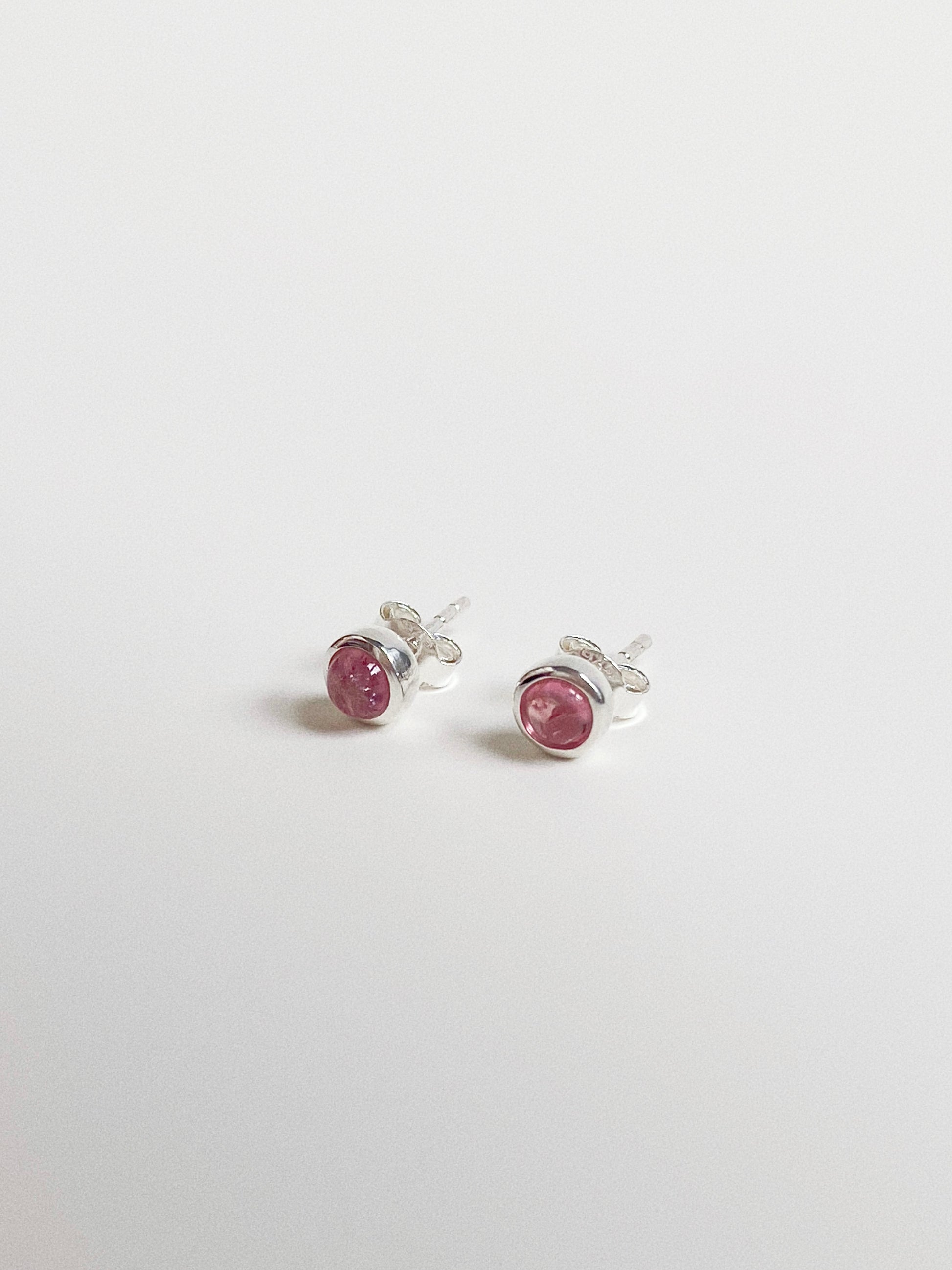 Angled view of rose pink tourmaline studs showing the smooth dome cabochon cut and silver bubble setting.