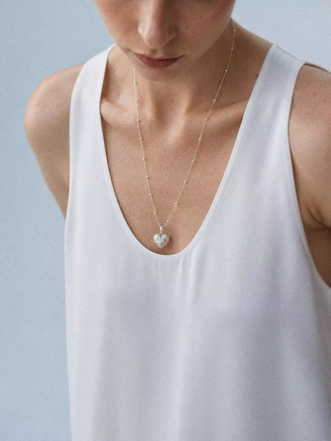 Model wearing the Bubble Heart pendant on its 60cm sterling silver bead chain with a white top.