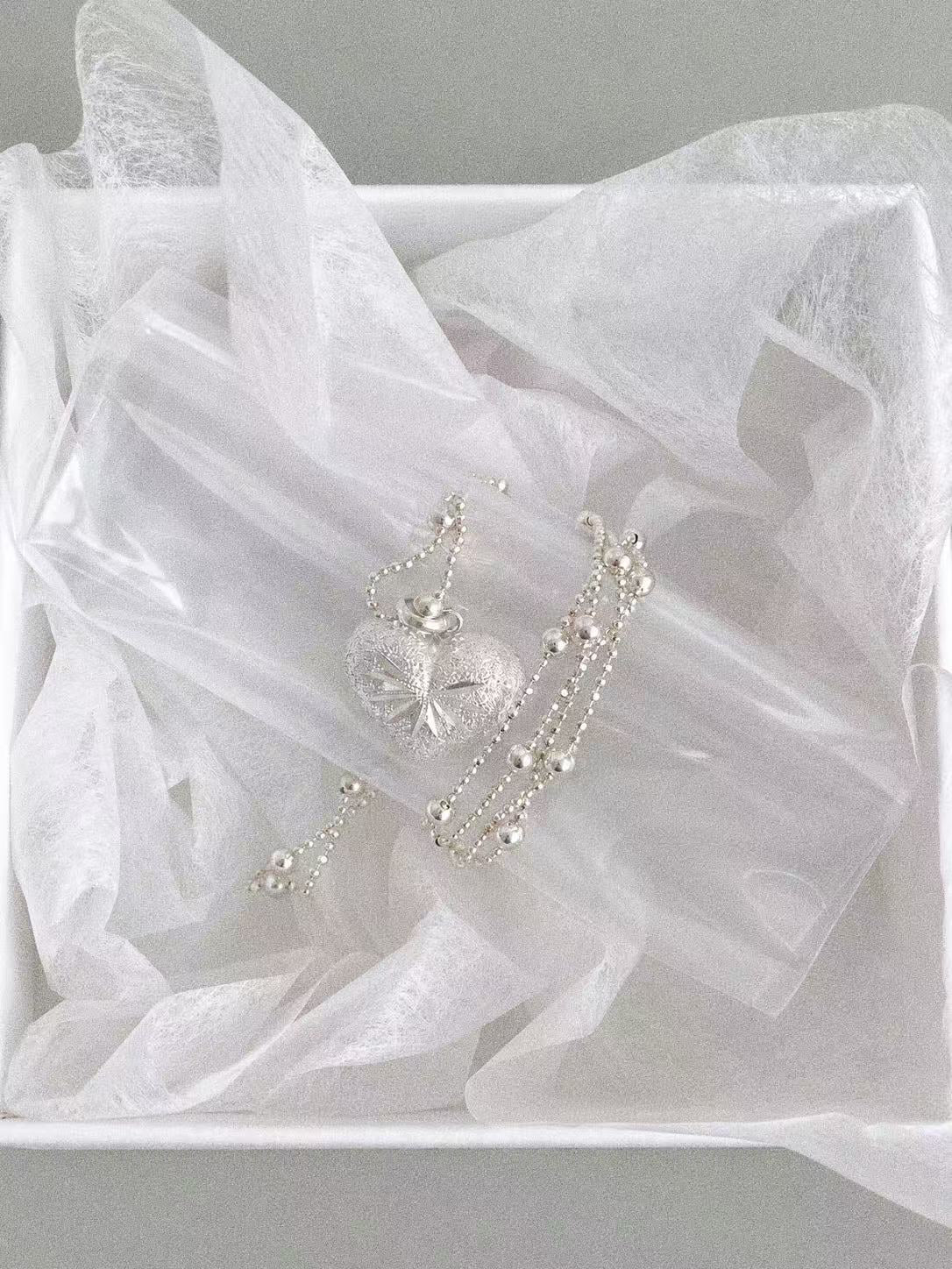 Close-up of the engraved silver heart pendant with faceted and smooth silver beads in a white jewellery box.