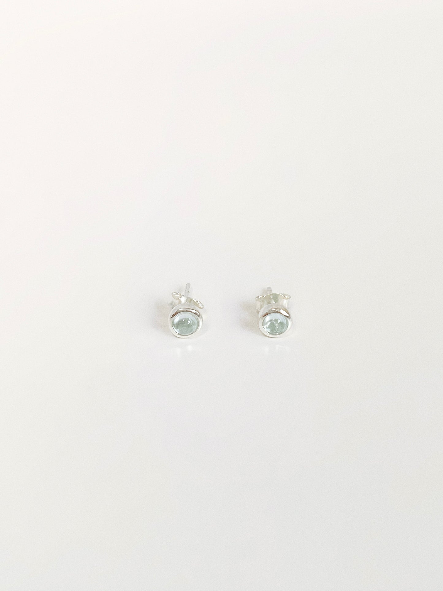 Natural blue topaz cabochon stud earrings in 925 sterling silver bezel flat lay by Deja Vu Jewellery