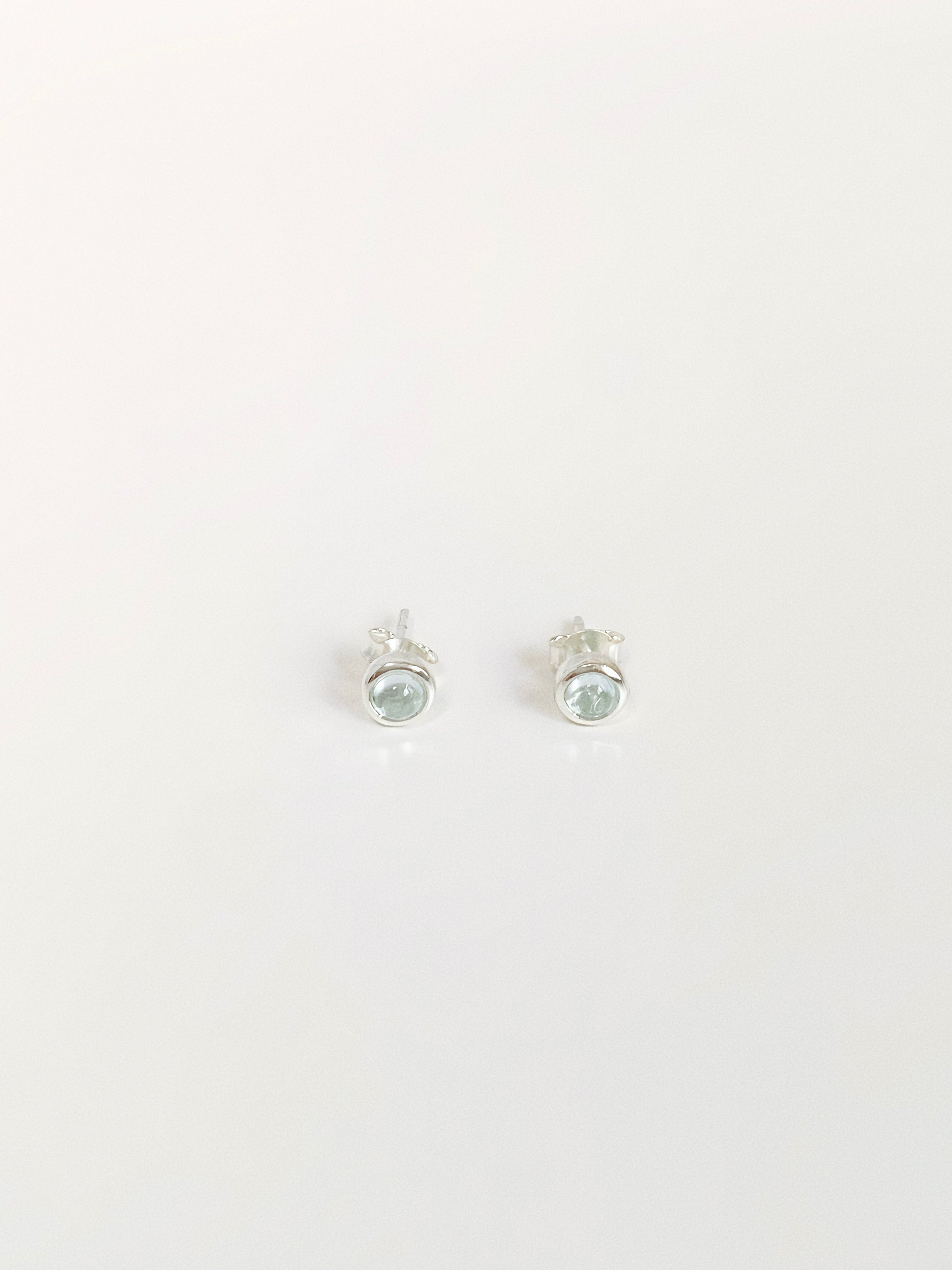 Natural blue topaz cabochon stud earrings in 925 sterling silver bezel flat lay by Deja Vu Jewellery