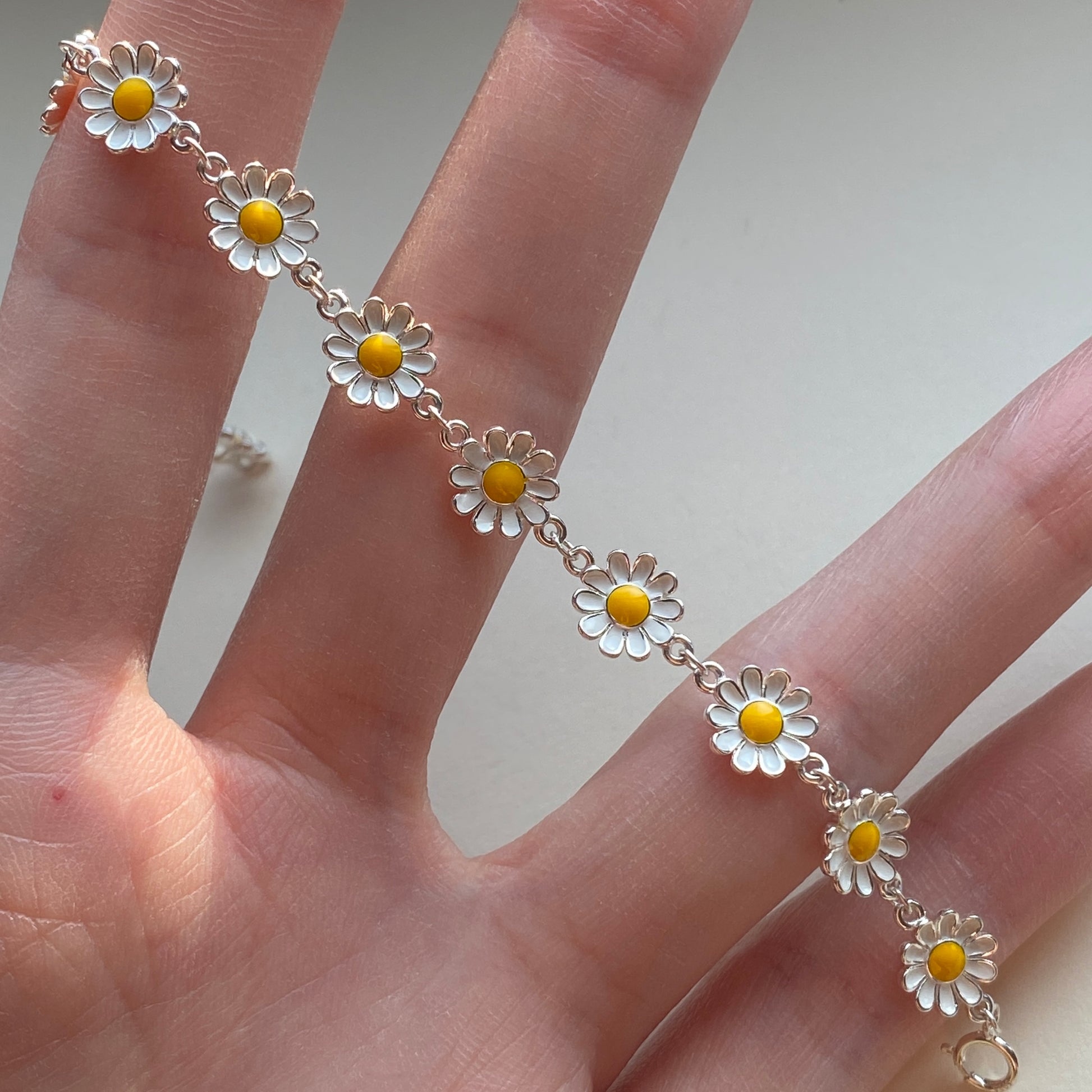 Close-up of white enamel daisies and yellow centers on silver bracelet