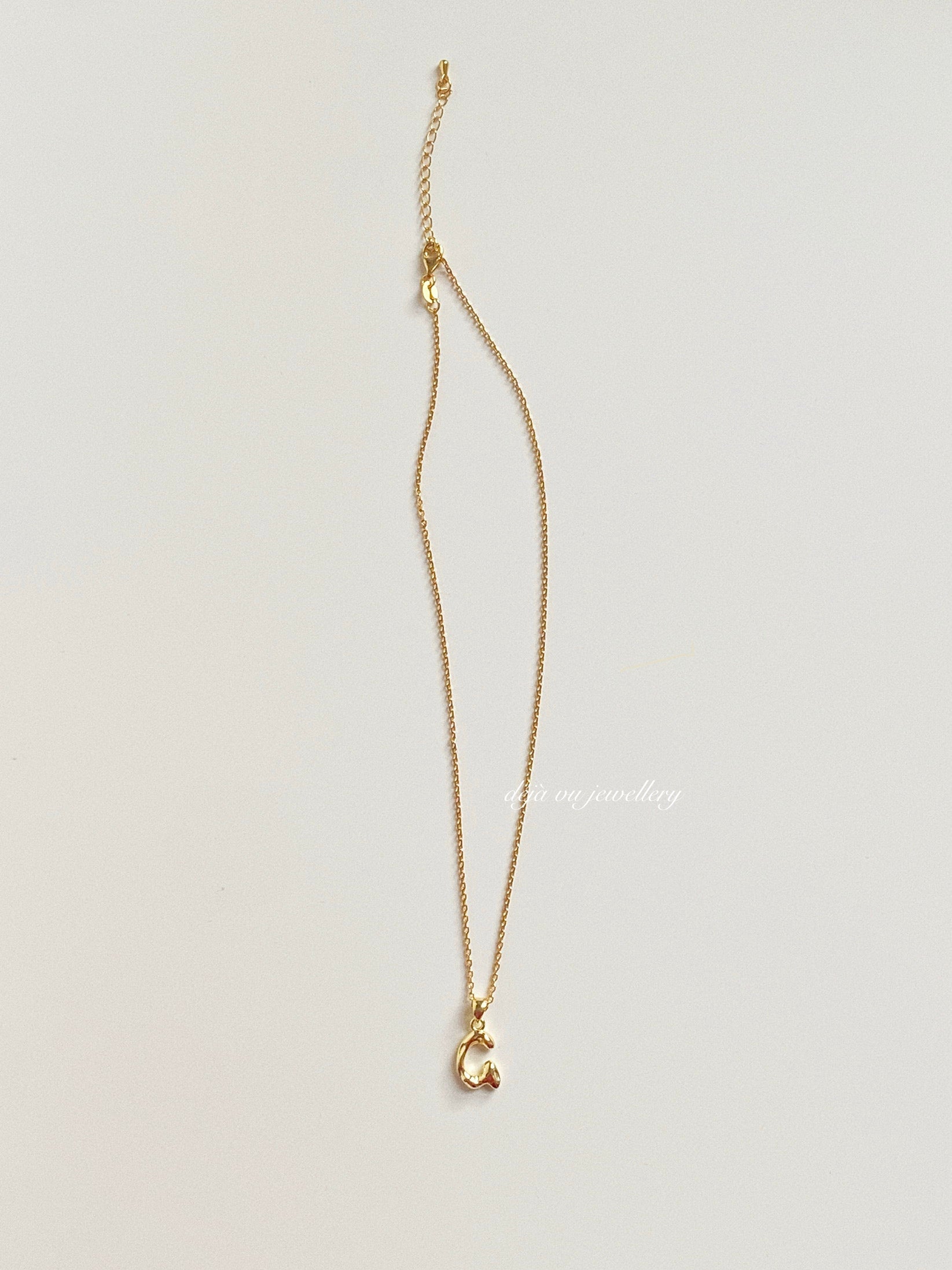 Gold vermeil letter G necklace lying flat on white surface, showing chain and pendant connection.