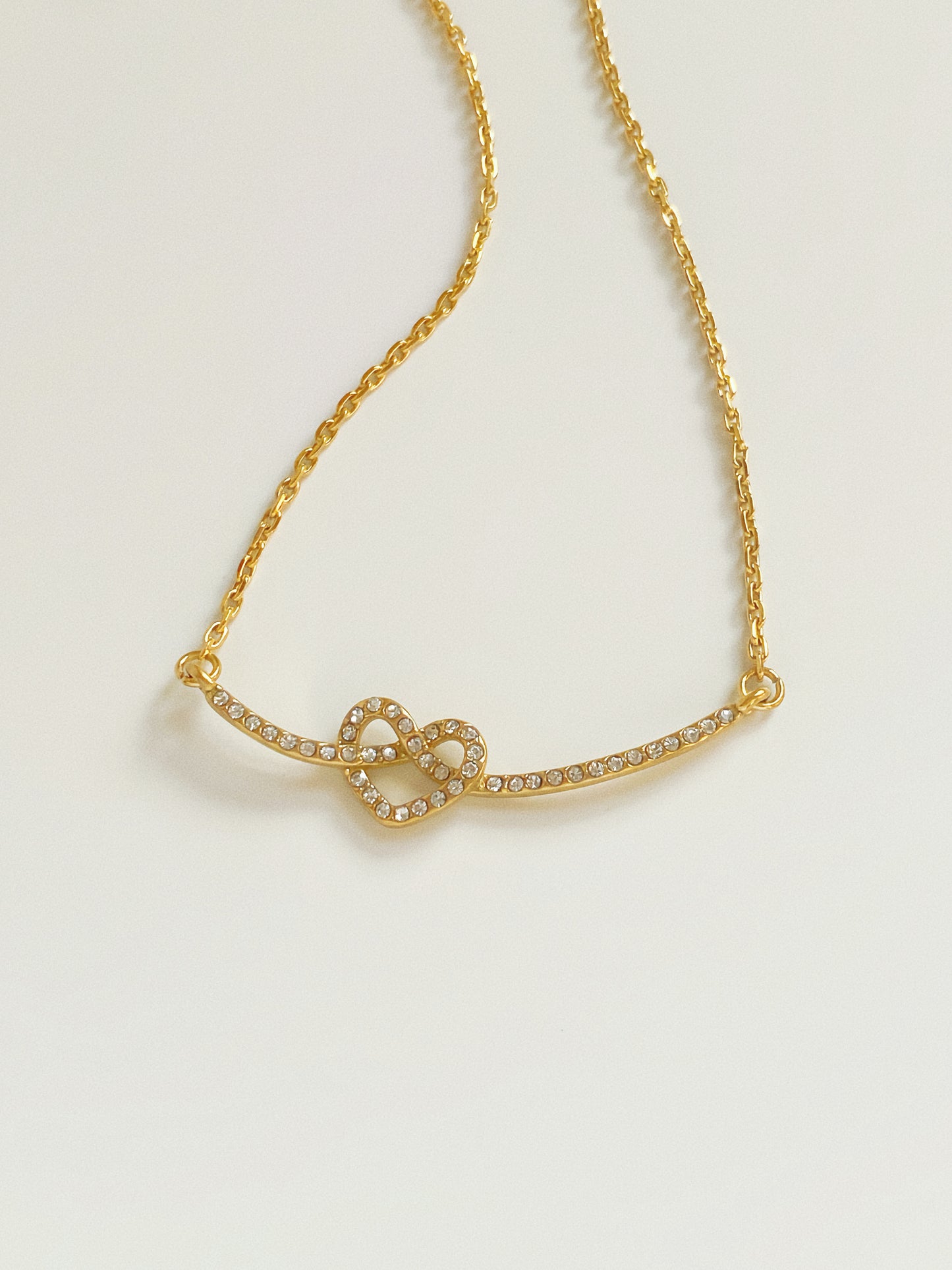 Aesthetic shot of gold curved bar necklace with heart knot detail, reflecting light to show high-quality gold plating.